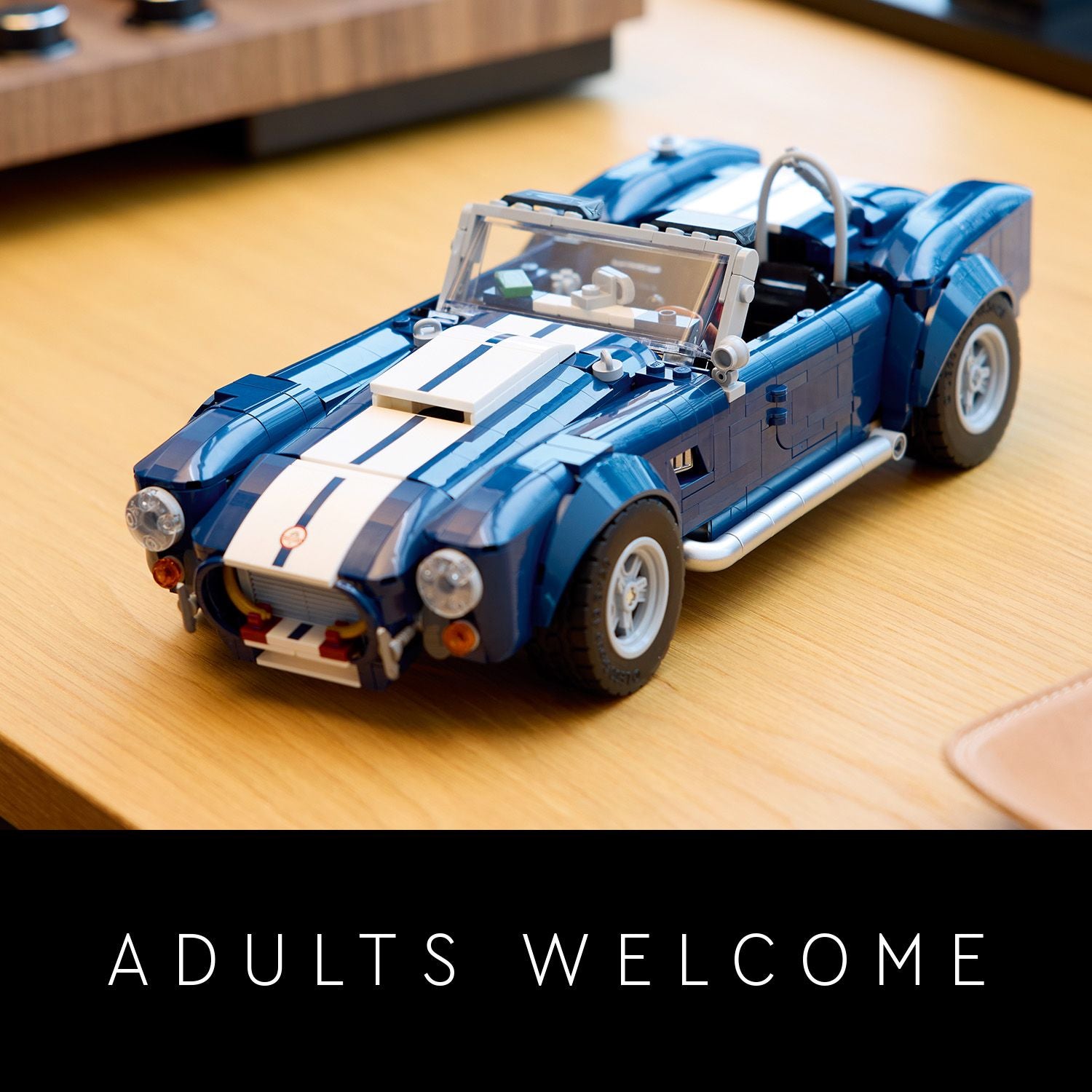 Modell des blauen LEGO Shelby Cobra 427 mit weißen Rennstreifen auf einem Holztisch, darunter Text 'ADULTS WELCOME'.