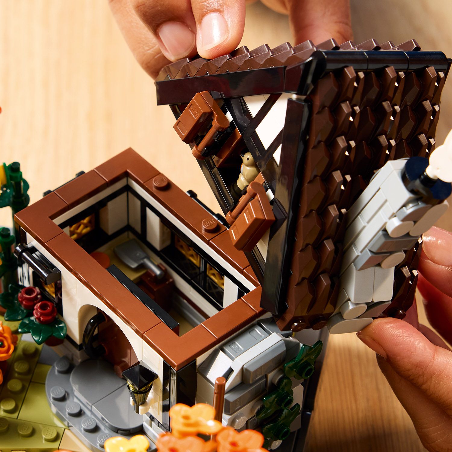 Hand hebt das abnehmbare, braune Dach eines LEGO Herbstlichen Landhausgartens mit sichtbarem Dachfenster und Innenraumdetails.