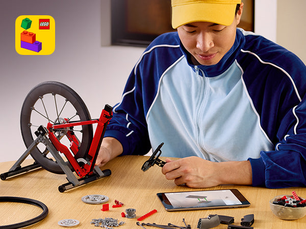 Person baut ein rotes LEGO Rennrad-Modell auf einem Tisch mit Tablet und LEGO Teilen