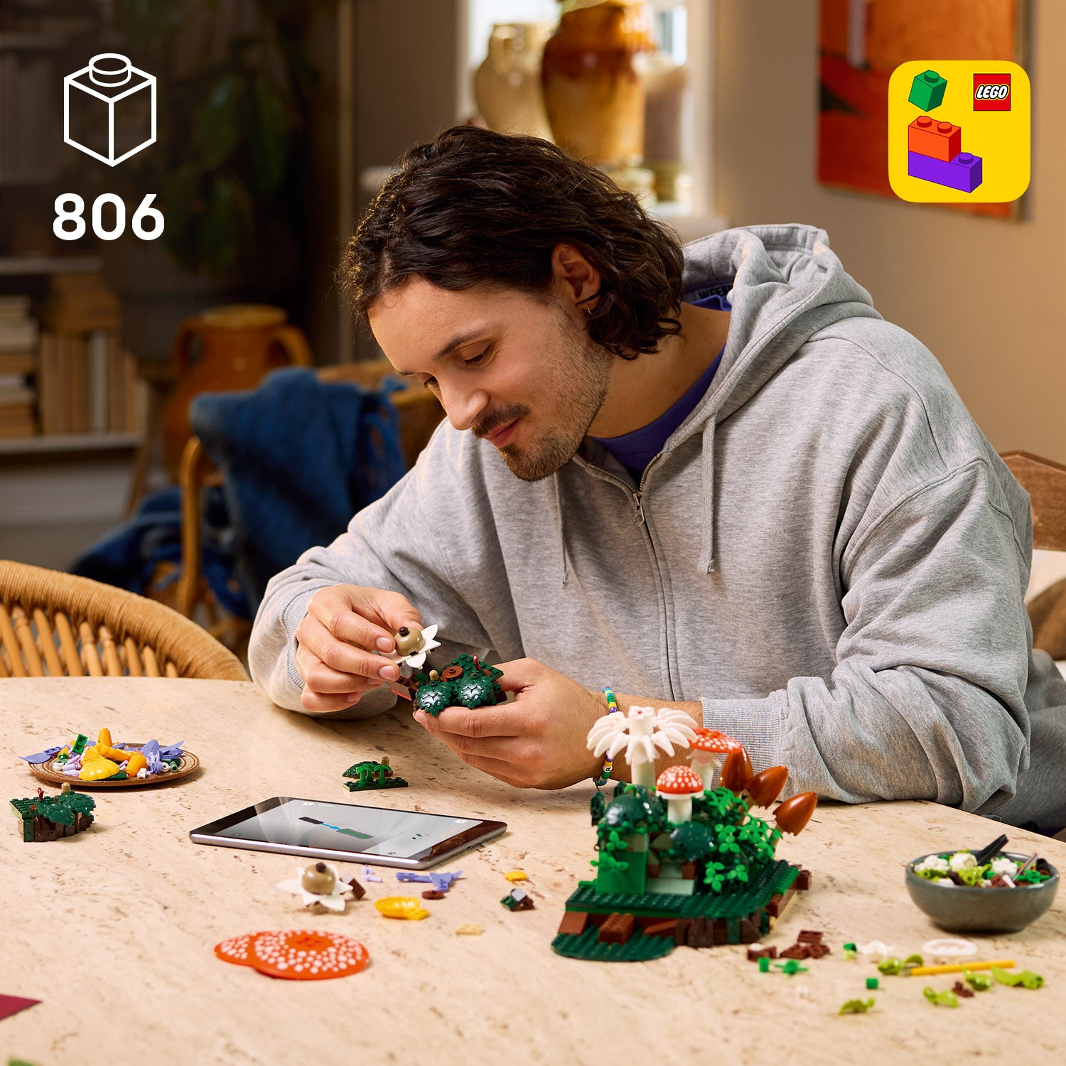 Mann mit grauem Kapuzenpullover sitzt an einem Tisch und baut mit LEGO Steinen ein Pilzmodell