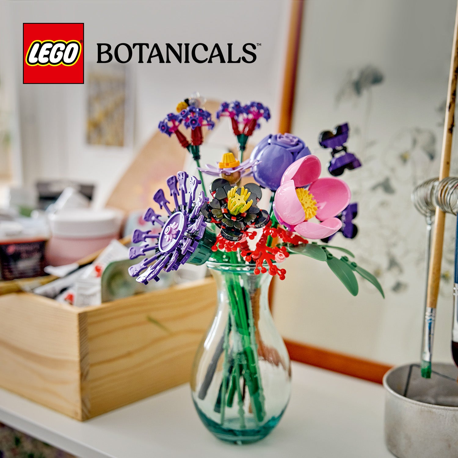 Vase mit einem bunten LEGO Blumenstrauß aus der LEGO Botanicals Serie auf einem weißen Tisch vor einem Spiegel und einem Holzkasten