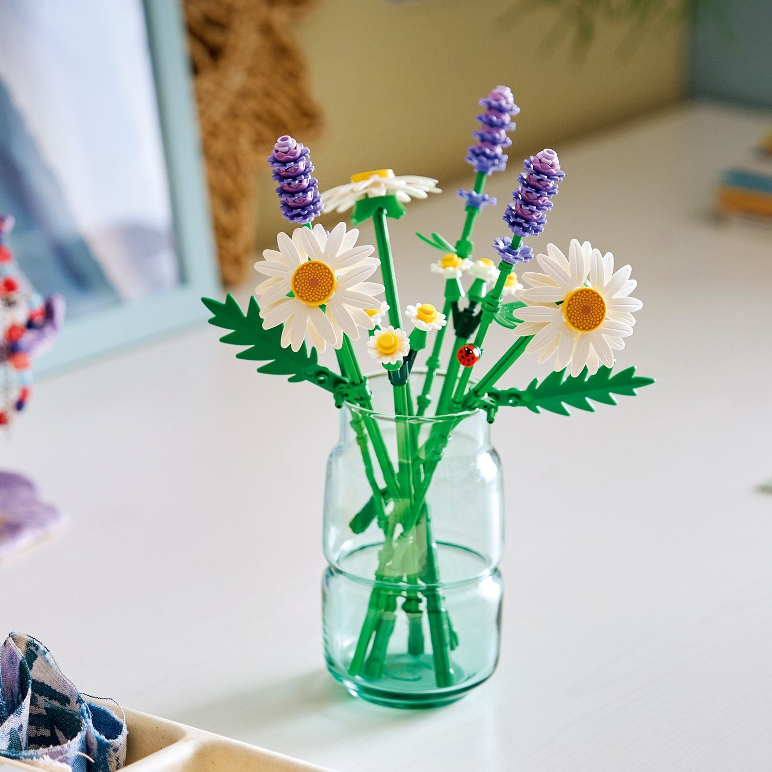 Vase mit LEGO Gänseblümchen und Lavendel aus der LEGO Botanicals Serie auf einem weißen Tisch.