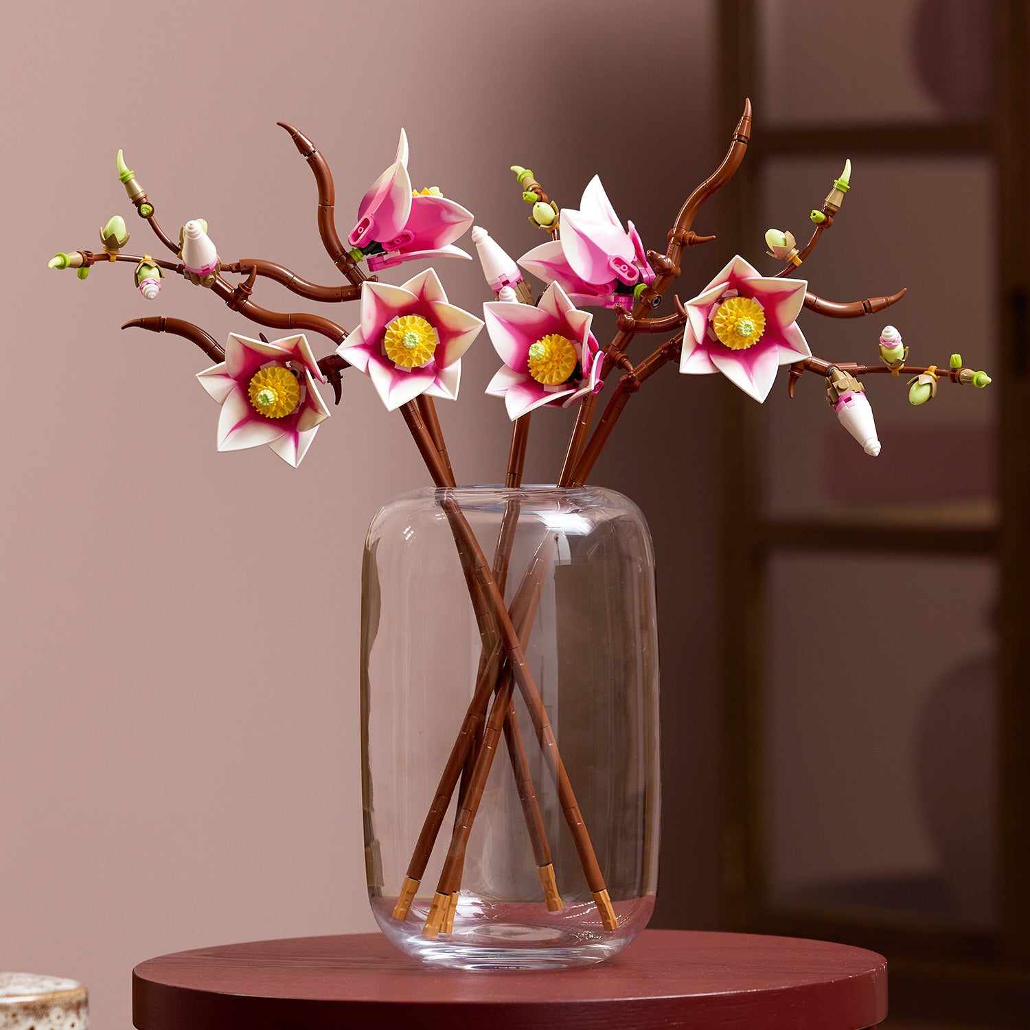 Klarglasvase mit mehreren braunen LEGO Zweigen, die pink-weiße Magnolienblüten mit gelben Blütenstempeln tragen