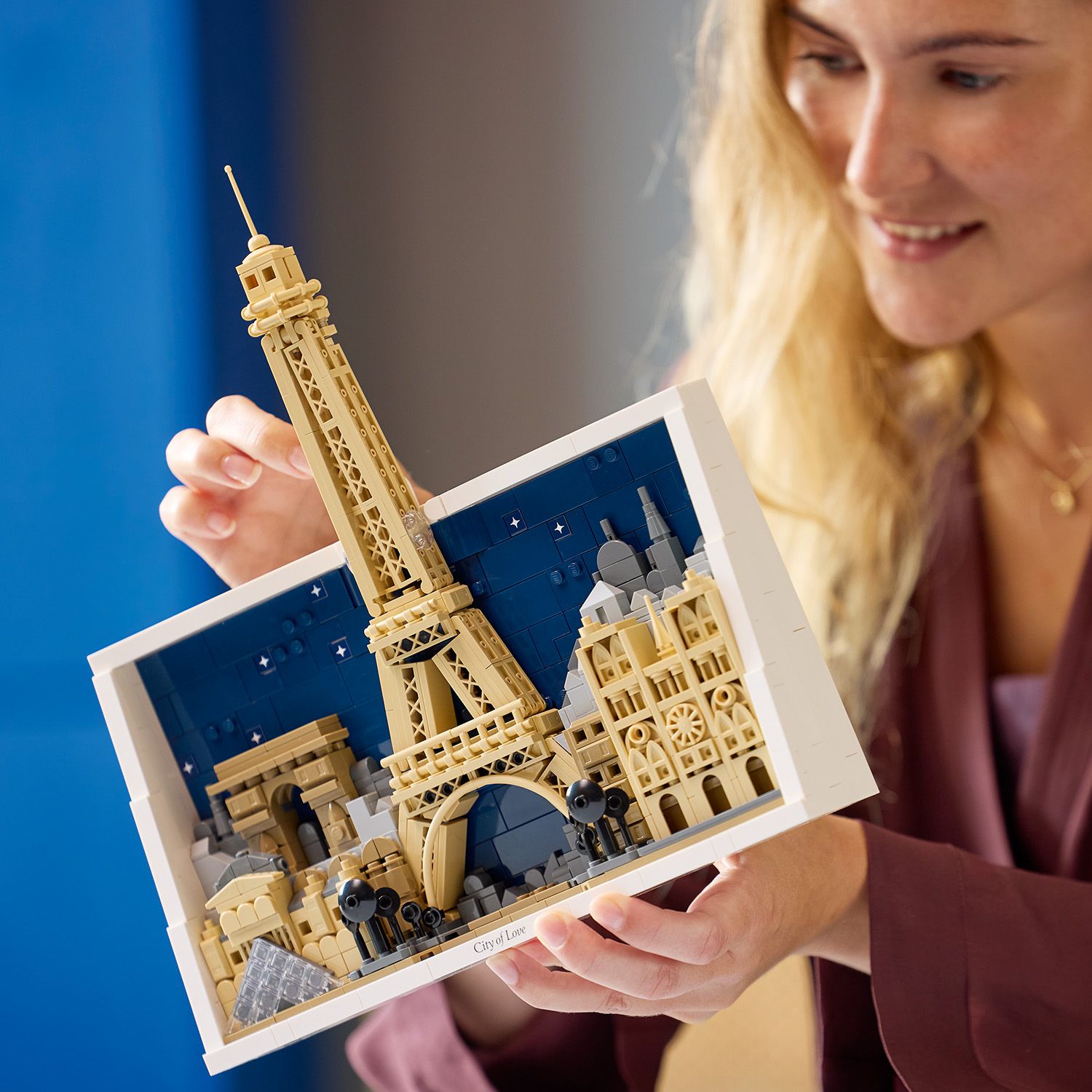 LEGO Architekturmodell von Paris mit Eiffelturm, Louvre-Pyramide, Triumphbogen und weiteren Wahrzeichen in einem weißen Rahmen vor blauem Hintergrund.