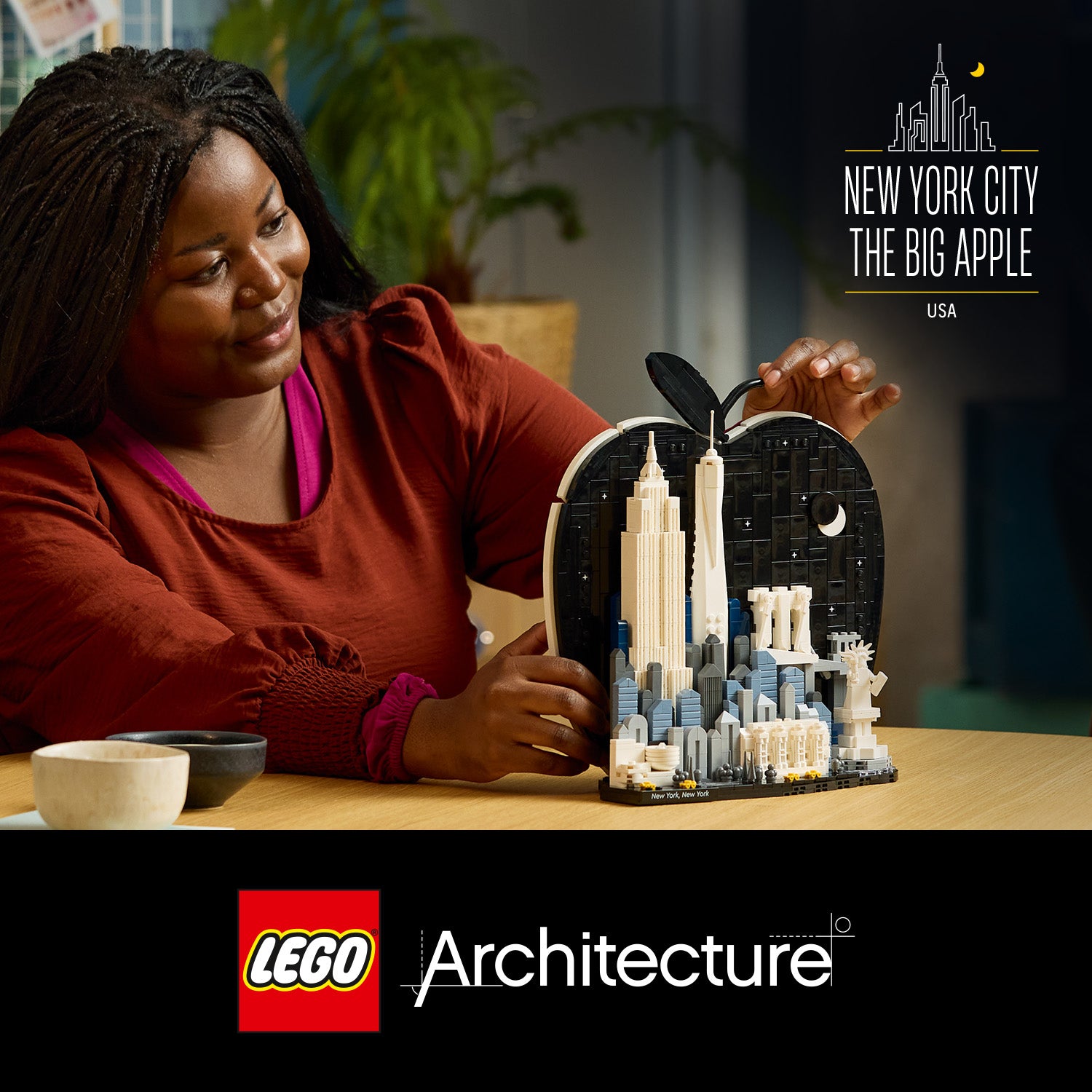 Person hält ein LEGO Architecture Set mit Miniaturgebäuden von New York City in einer Apfelförmigen Hülle