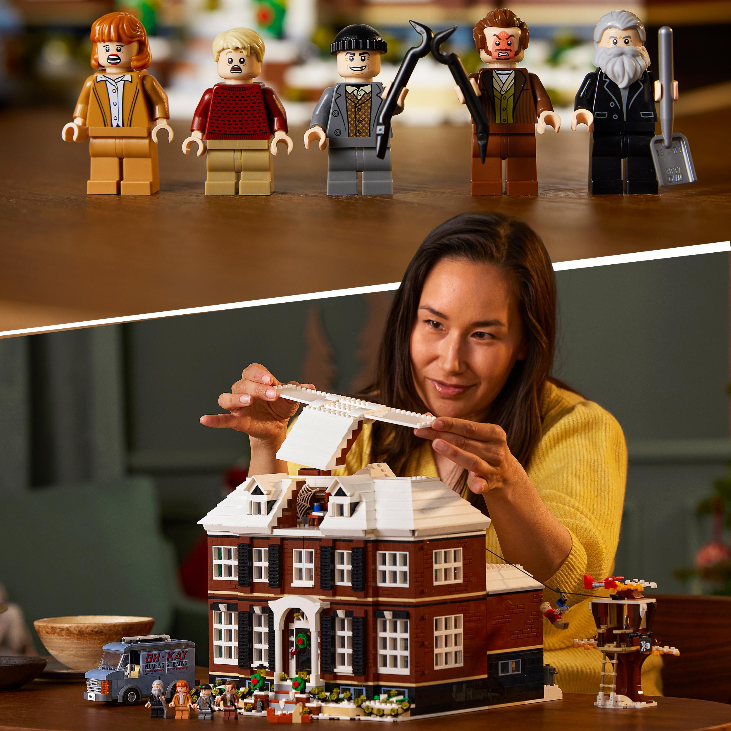Fünf LEGO-Minifiguren aus dem Set "21330 LEGO Home Alone" stehen nebeneinander, darunter zwei mit Werkzeugen. Darunter baut eine Person ein detailreiches LEGO-Haus mit braunen und weißen Bauteilen.