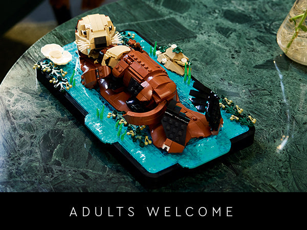 LEGO Modell eines schwimmenden Otters auf blauem Wasser mit Pflanzen auf grünem Untergrund