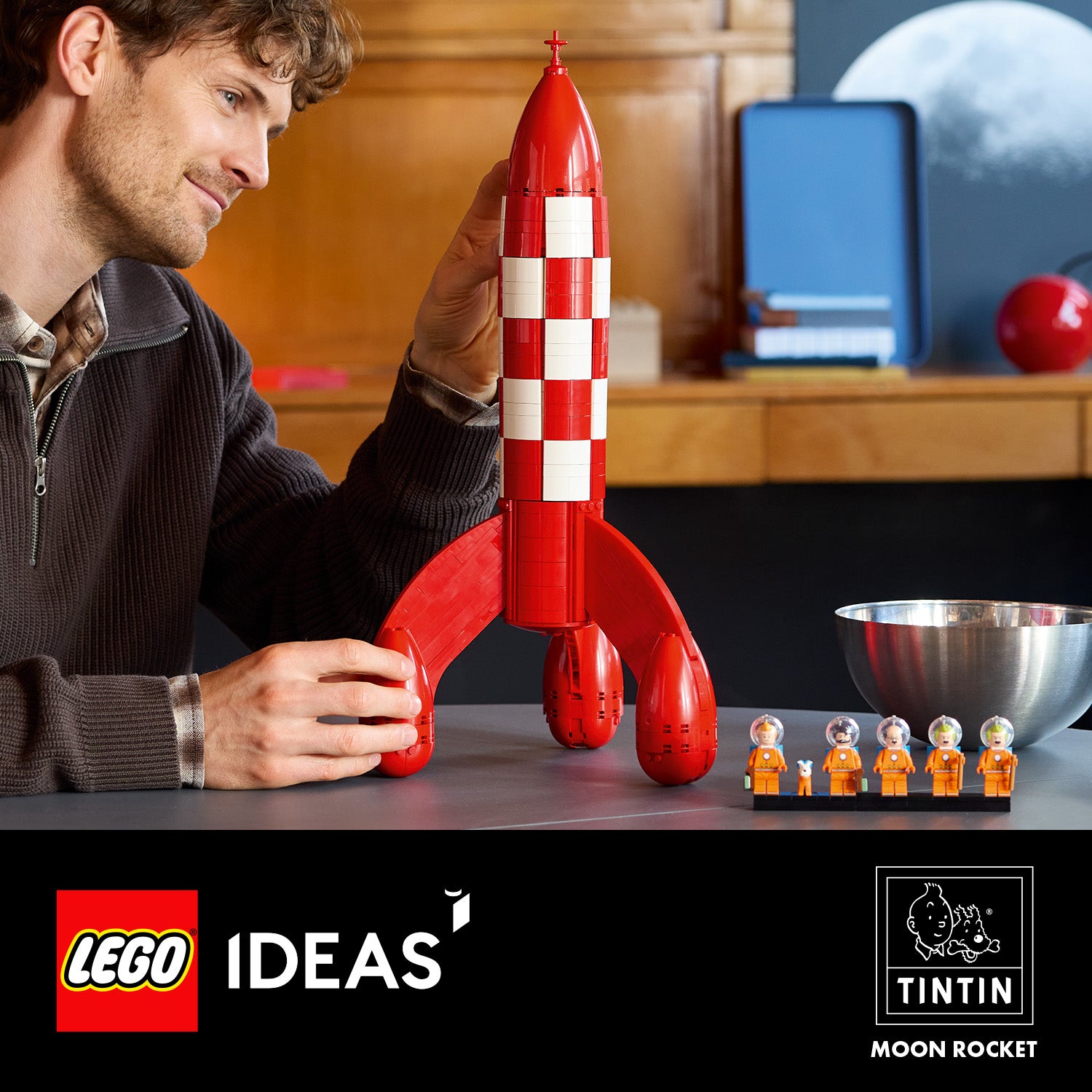 Mann baut rote und weiße LEGO Rakete mit fünf kleinen Astronautenfiguren auf grauem Tisch