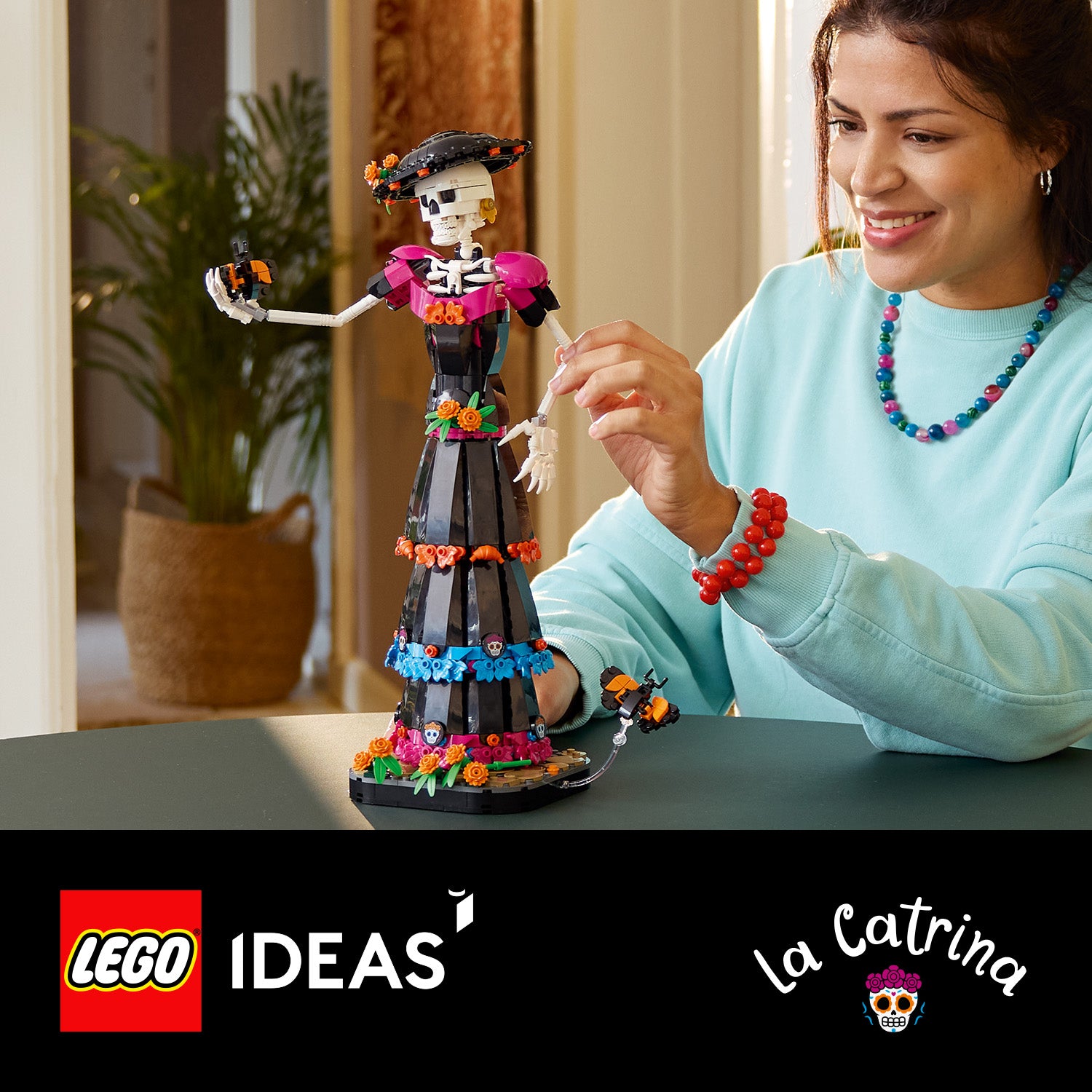 Frau mit buntem Schmuck spielt mit einer detailreichen LEGO La-Catrina-Figur in traditionellem Kleid und Hut auf einem Tisch