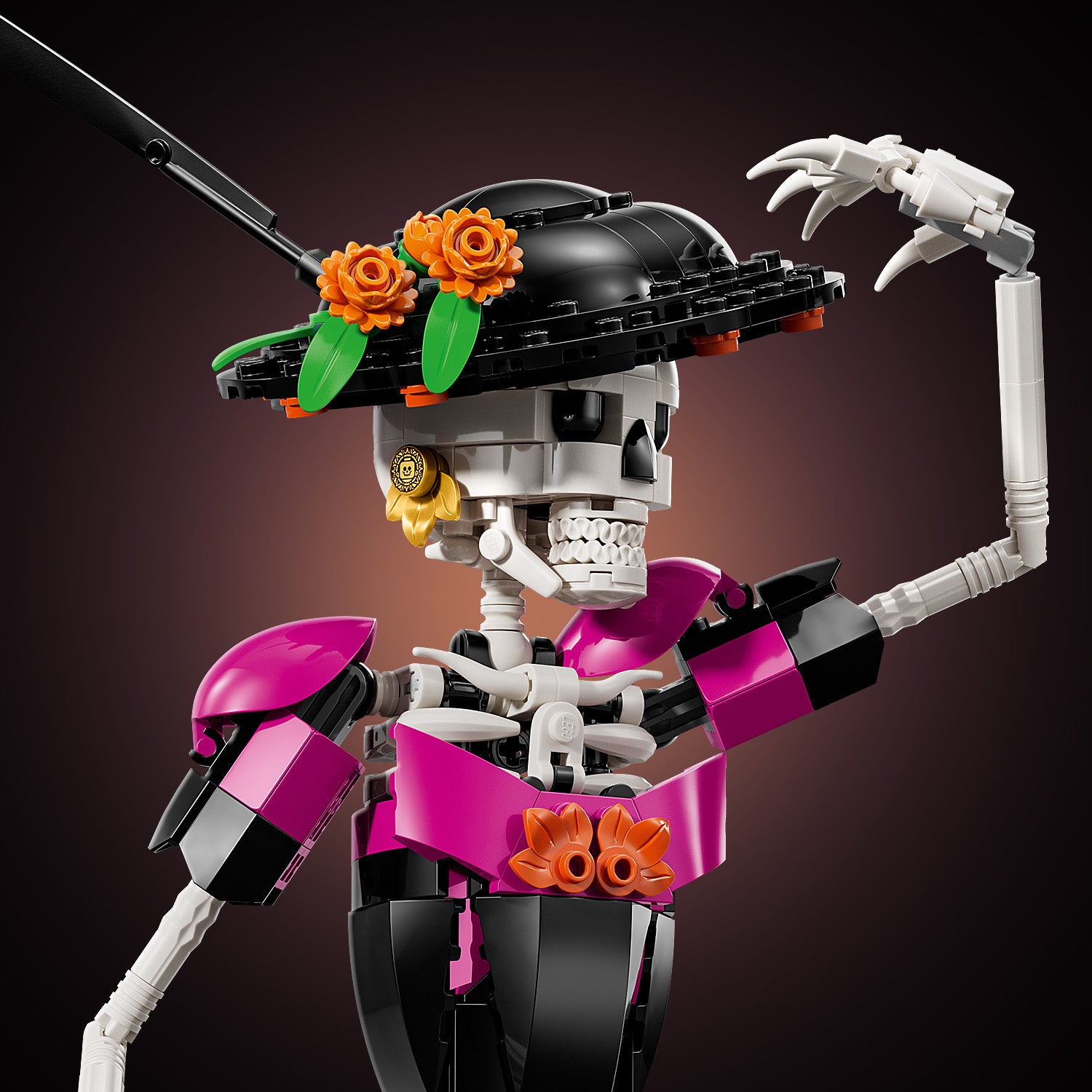 LEGO Skelettfigur mit schwarzem Hut, orangefarbenen Blumen und pink-schwarzen Details, die den Arm hebt