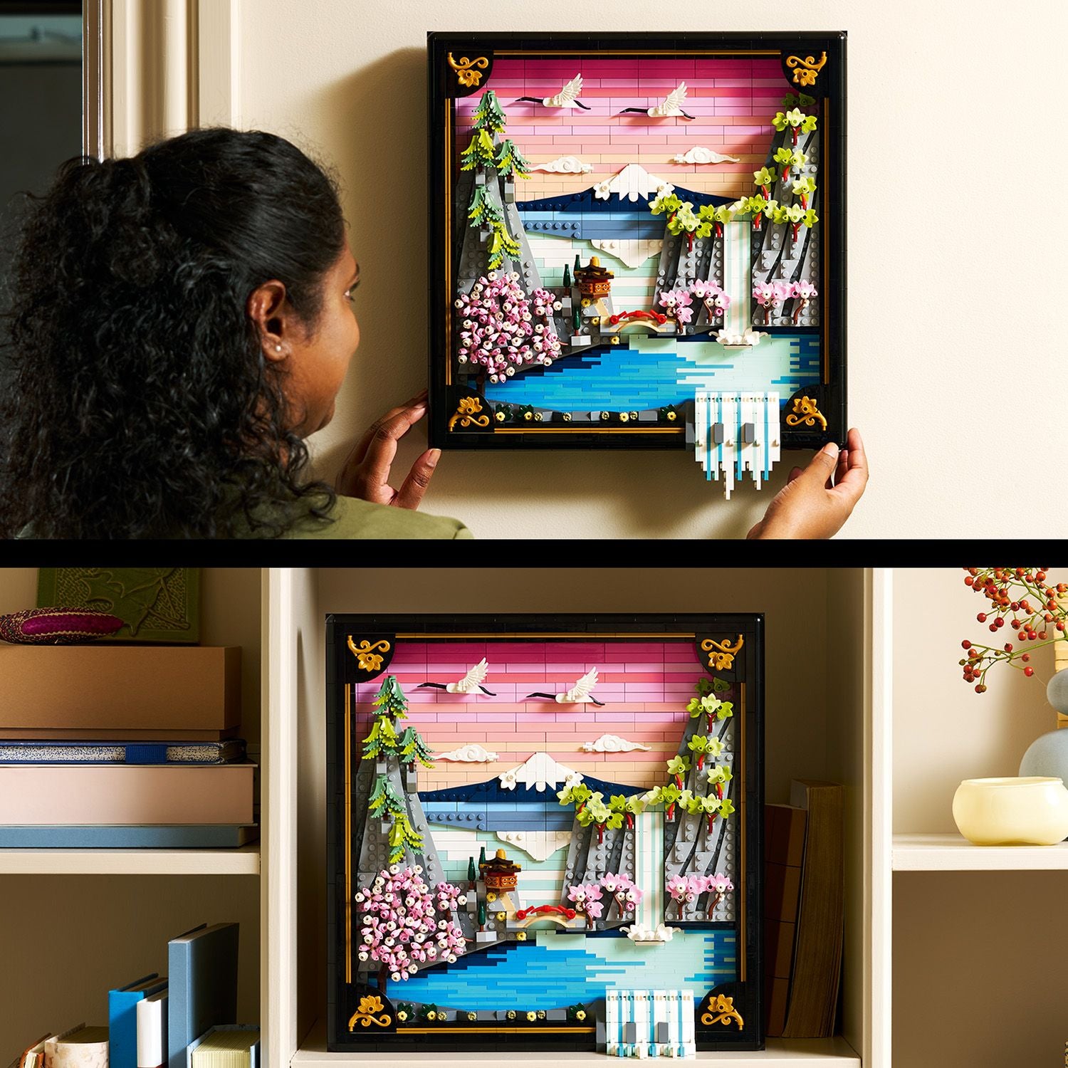 Eine Person hält ein quadratisches LEGO Kunstwerk mit japanischer Kirschblütenlandschaft, das Berge, Wasser, Kirschblütenbäume, Kraniche und einen Tempel zeigt, eingerahmt in einem schwarzen Rahmen mit goldenen Verzierungen.