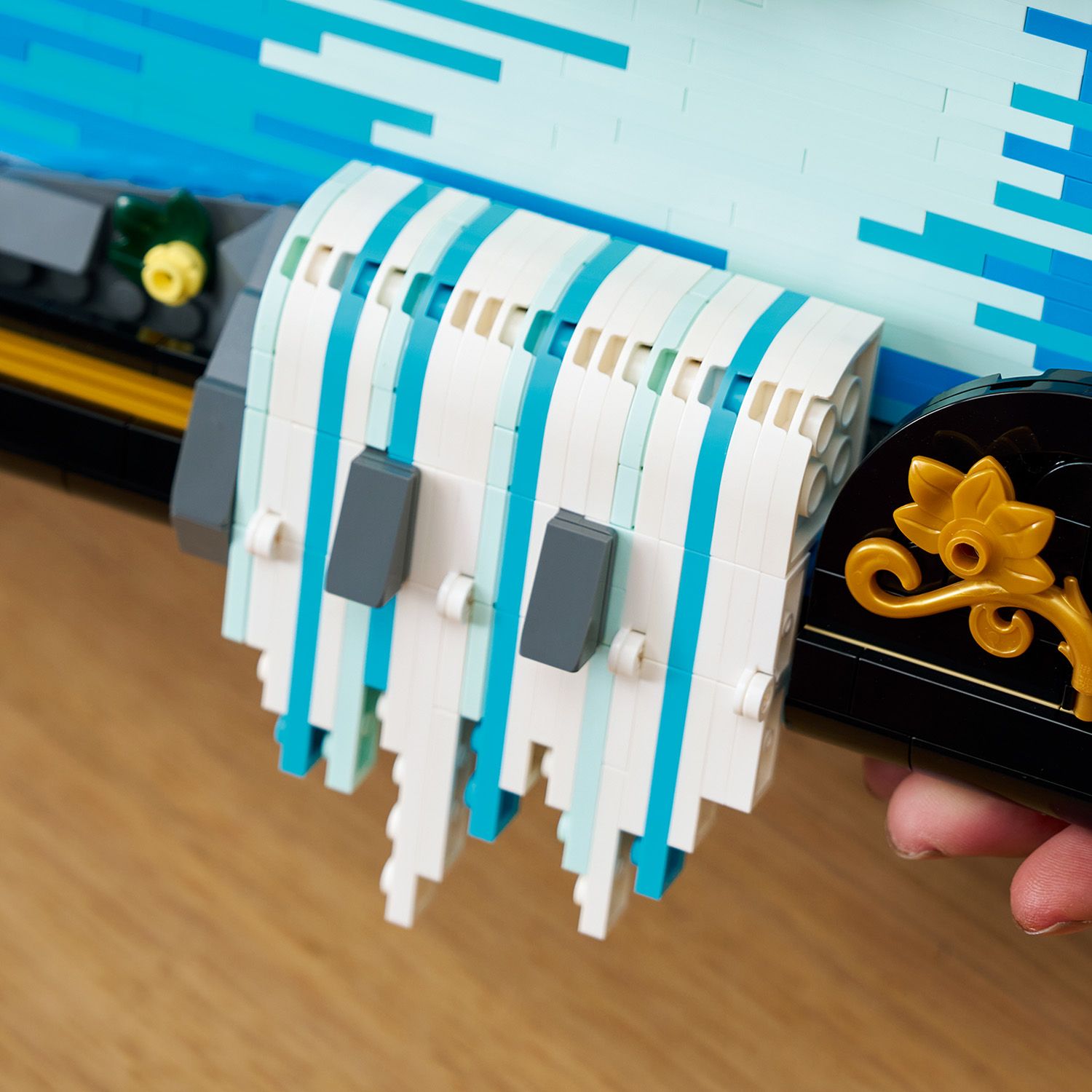 Nahaufnahme eines LEGO Modells mit weißen und blauen vertikalen Streifen, grauen rechteckigen Elementen und goldfarbenen Verzierungen, gehalten von einer Hand.