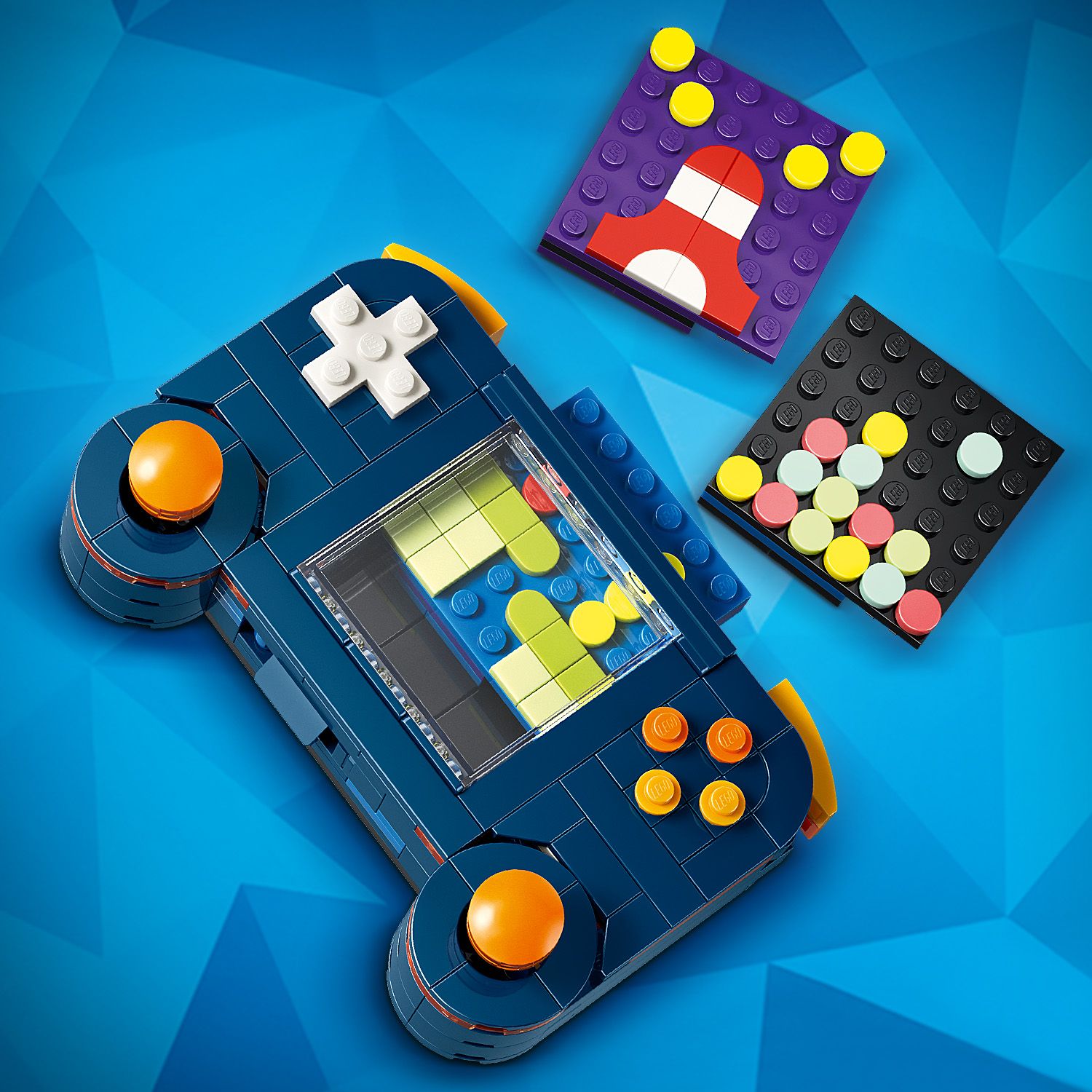 Blaue LEGO Retro-Spielkonsole mit zwei orangen Joysticks, einem weißen Steuerkreuz und einem kleinen Bildschirm, daneben zwei bunte, quadratische LEGO Platten mit Mustern.