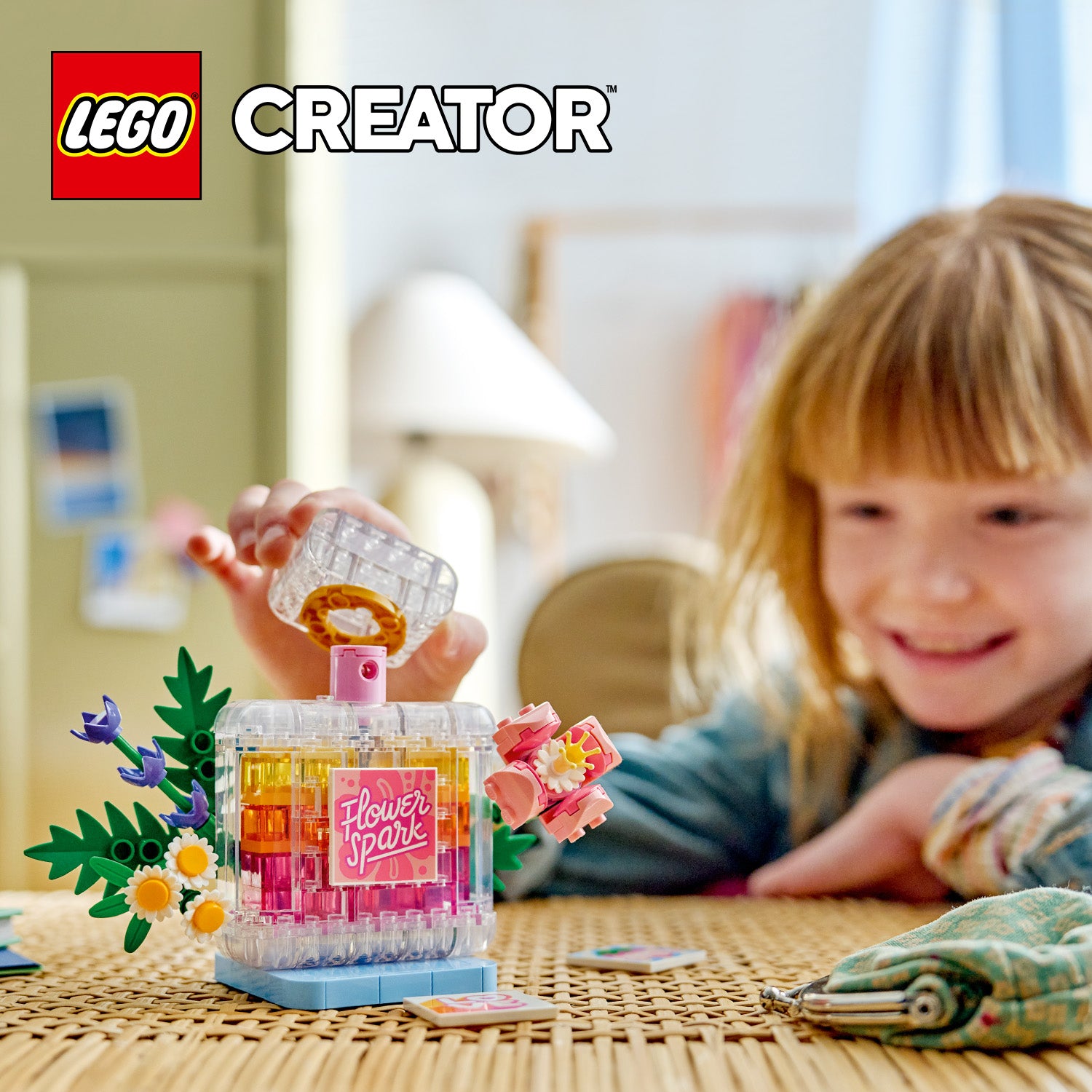 Kind spielt mit einer LEGO Parfümflasche mit Blumendekoration auf einem Tisch