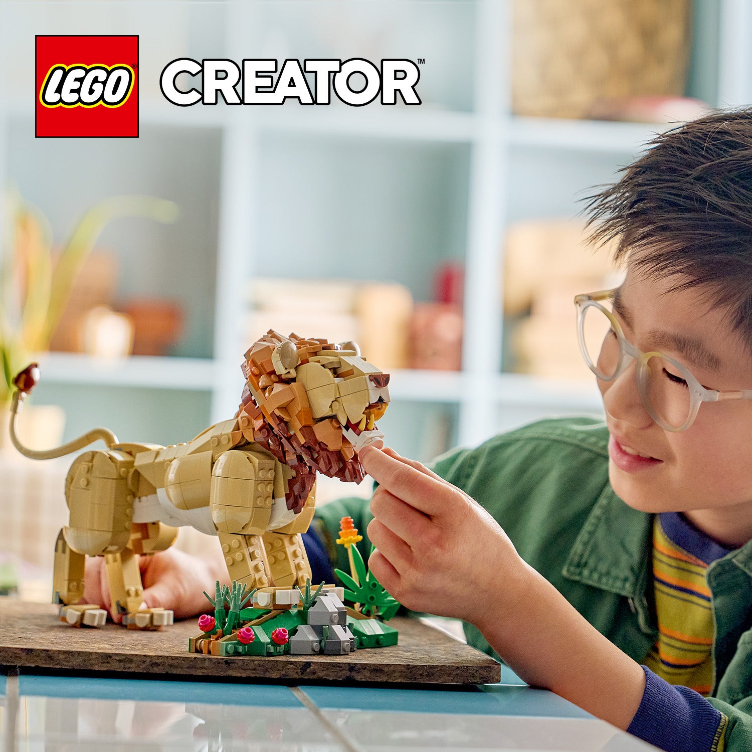 Kind baut mit LEGO Creator einen majestätischen Löwen aus braunen und beigen Bausteinen auf einem Sockel mit Pflanzen und Steinen