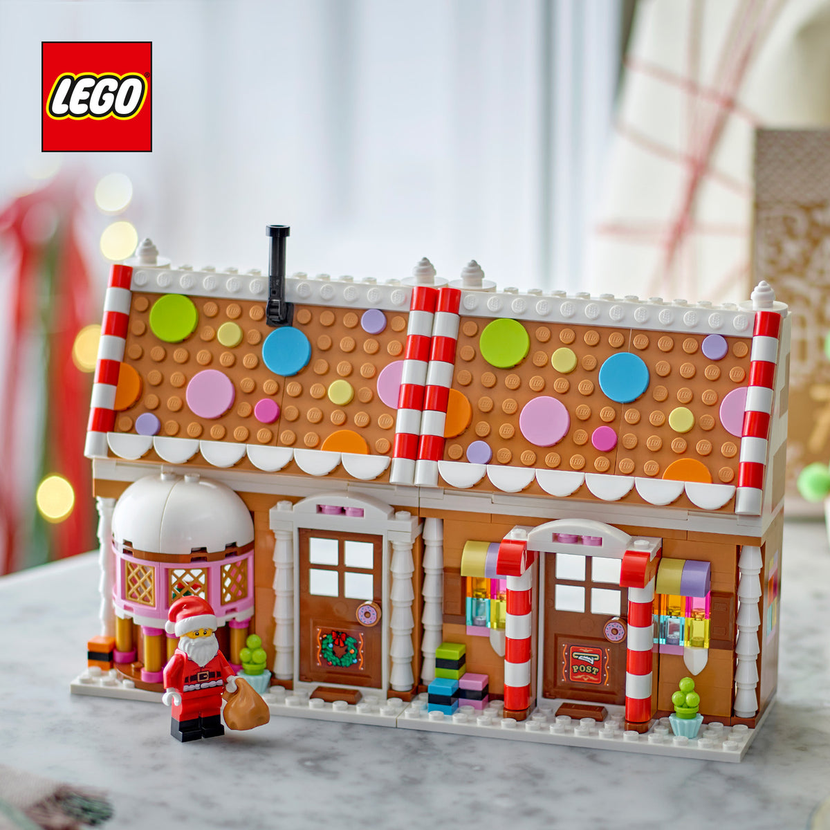 Weihnachtliches Lebkuchenhaus aus LEGO mit Zuckerstangen-Dach, bunten Kreisen und zwei Türen, davor eine LEGO Figur mit Sack