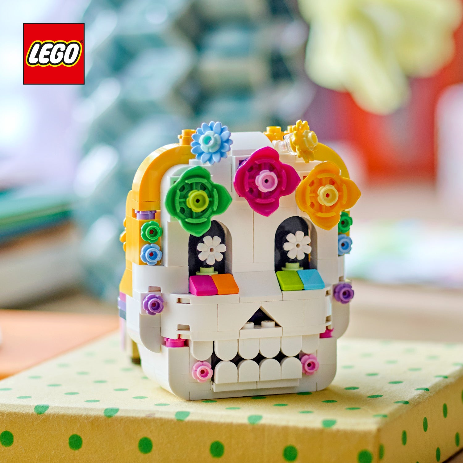 Bunter LEGO Schädel mit Blumenverzierungen auf einem gepunkteten Untergrund, links oben das LEGO Logo