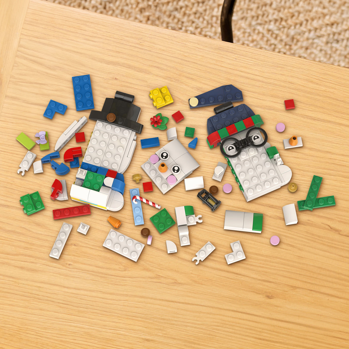 Drei teilweise zusammengesetzte Schneemänner aus LEGO Steinen auf einem Holztisch, umgeben von verstreuten bunten LEGO Teilen