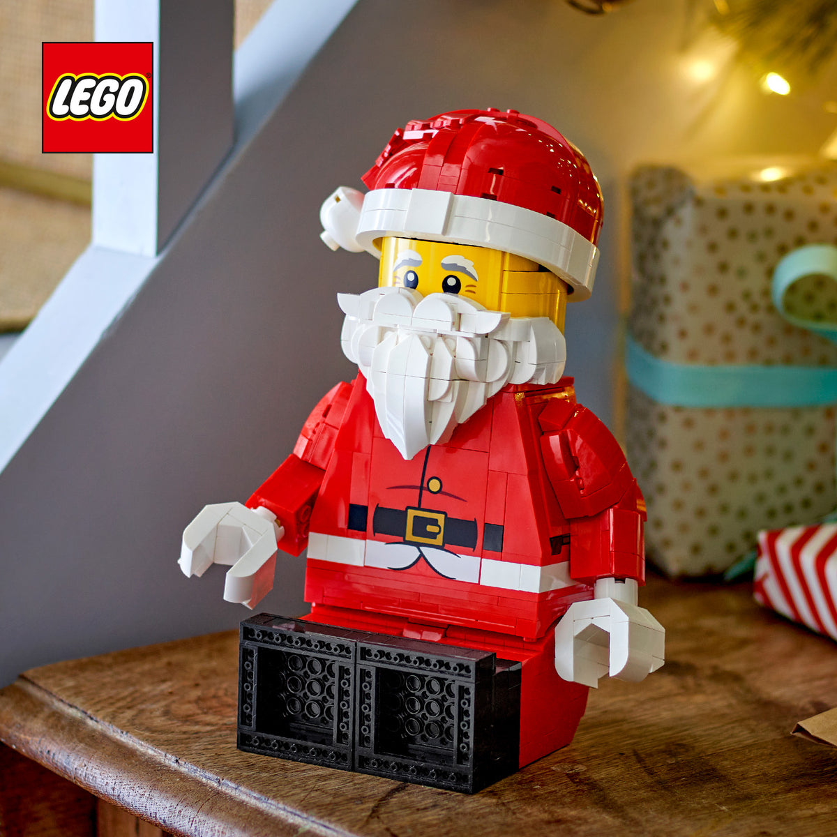 Große LEGO Weihnachtsmann-Minifigur mit rotem Mantel, weißem Bart und roter Mütze sitzt auf einem Holztisch