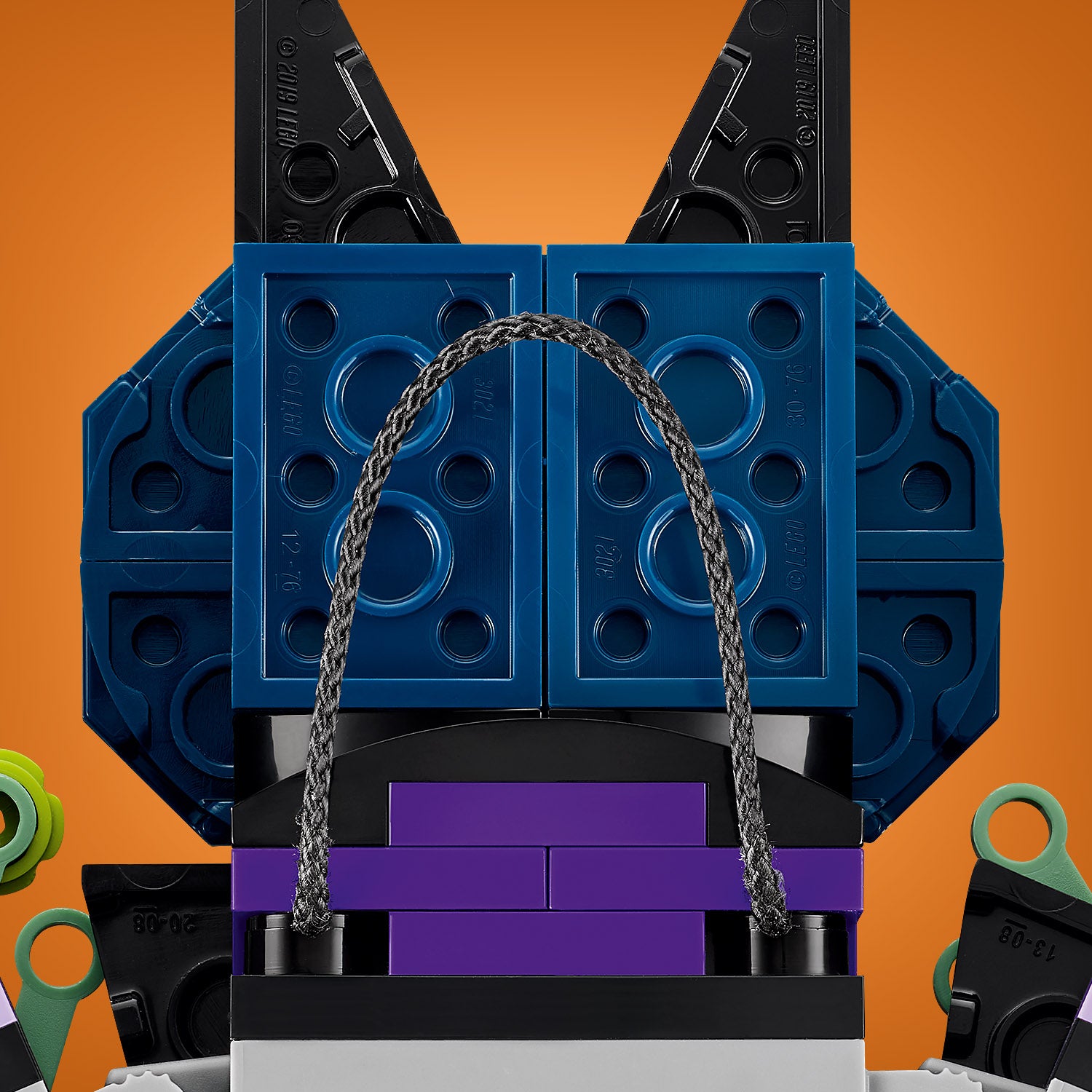 Nahaufnahme eines LEGO Halloweenkranzes mit schwarzen Fledermausflügeln, blauen quadratischen Elementen und einem violetten Streifen, der von einer grauen Kordel durchzogen ist