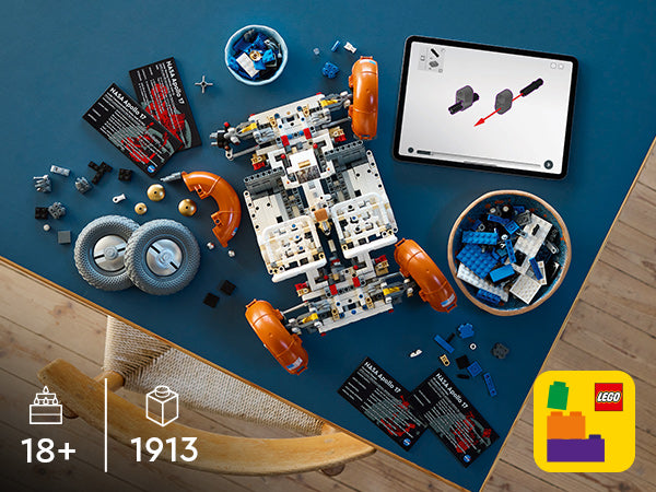 Teilweise zusammengebautes LEGO Technik-Modell des NASA Apollo Lunar Roving Vehicle mit verstreuten Bauteilen, Bauanleitung auf Tablet und LEGO Verpackung auf einem blauen Tisch