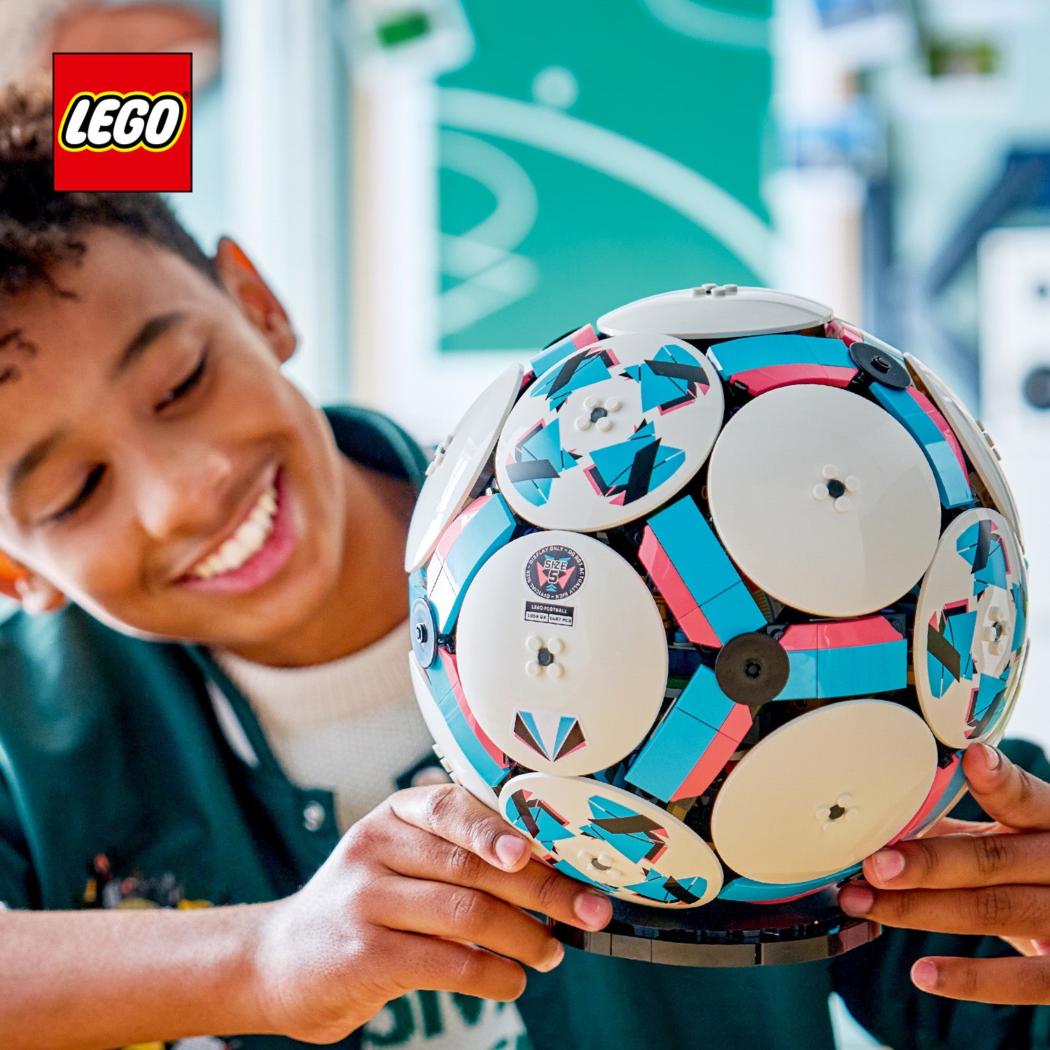 Person hält einen runden LEGO Fußball mit weißen, blauen und roten Elementen und einem schwarzen Ständer
