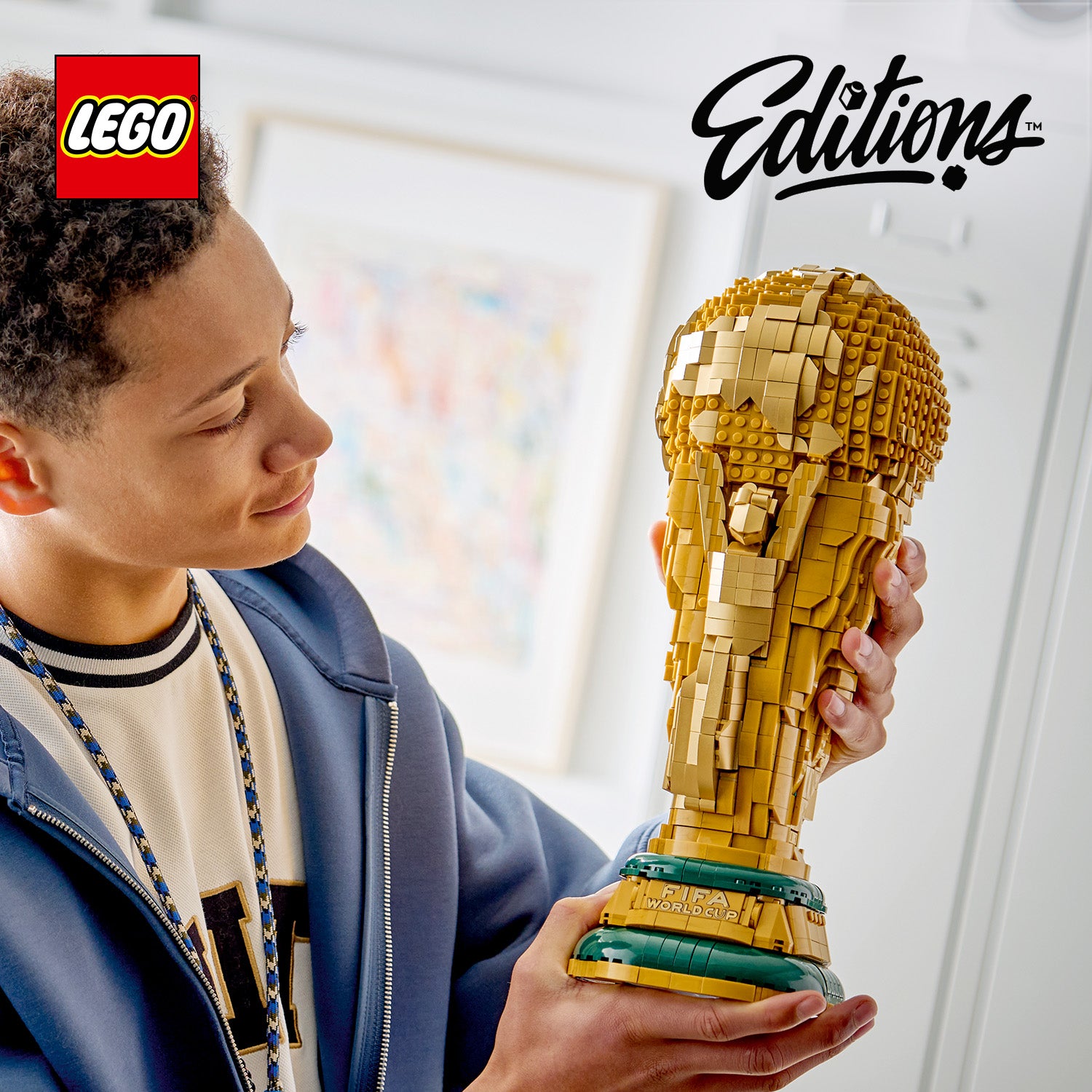 Kind hält LEGO Modell des FIFA-Weltmeisterschaftspokals aus goldfarbenen und grünen Bausteinen