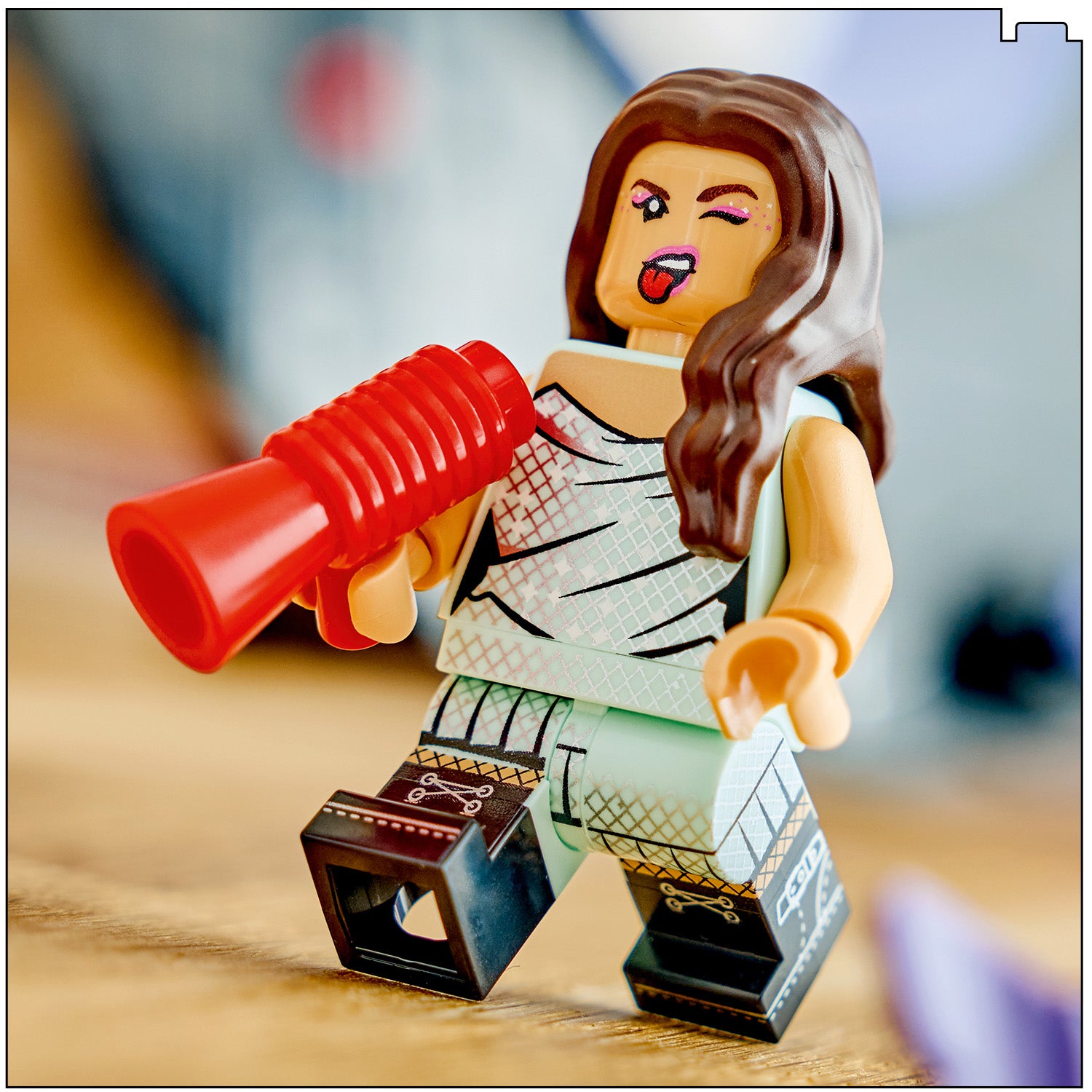 LEGO Figur von Olivia Rodrigo mit langem braunem Haar, die eine weiße, gemusterte Kleidung trägt und eine rote Megafon-Requisite hält, mit zwinkerndem Gesicht und herausgestreckter Zunge