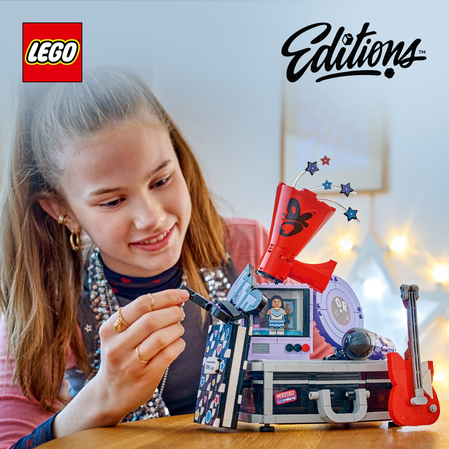 Ein Mädchen spielt mit einem LEGO Set, das einen Koffer mit einem roten Lautsprecher, einer Gitarre und einem kleinen Minifigurenbildschirm zeigt.