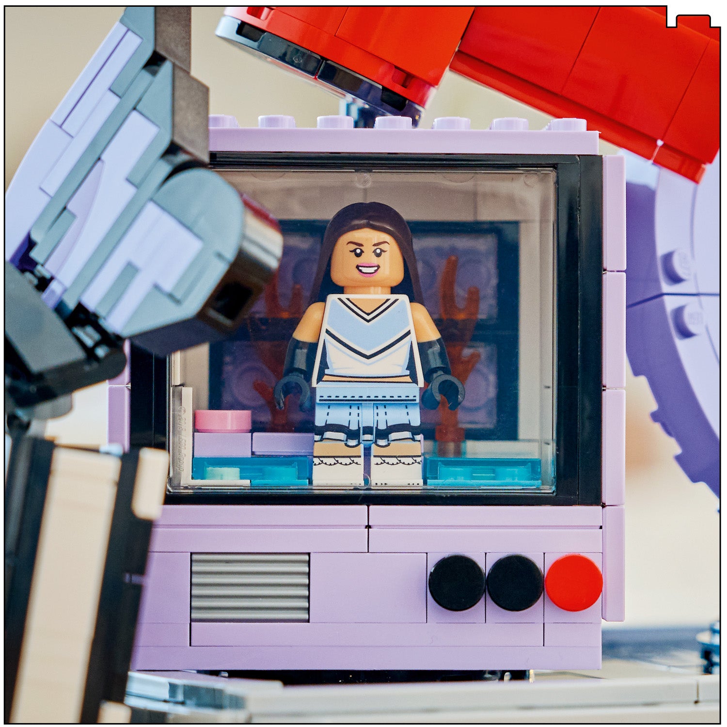LEGO Minifigur von Olivia Rodrigo in einem lilafarbenen Koffer mit schwarzen und roten Knöpfen, umgeben von LEGO Teilen.