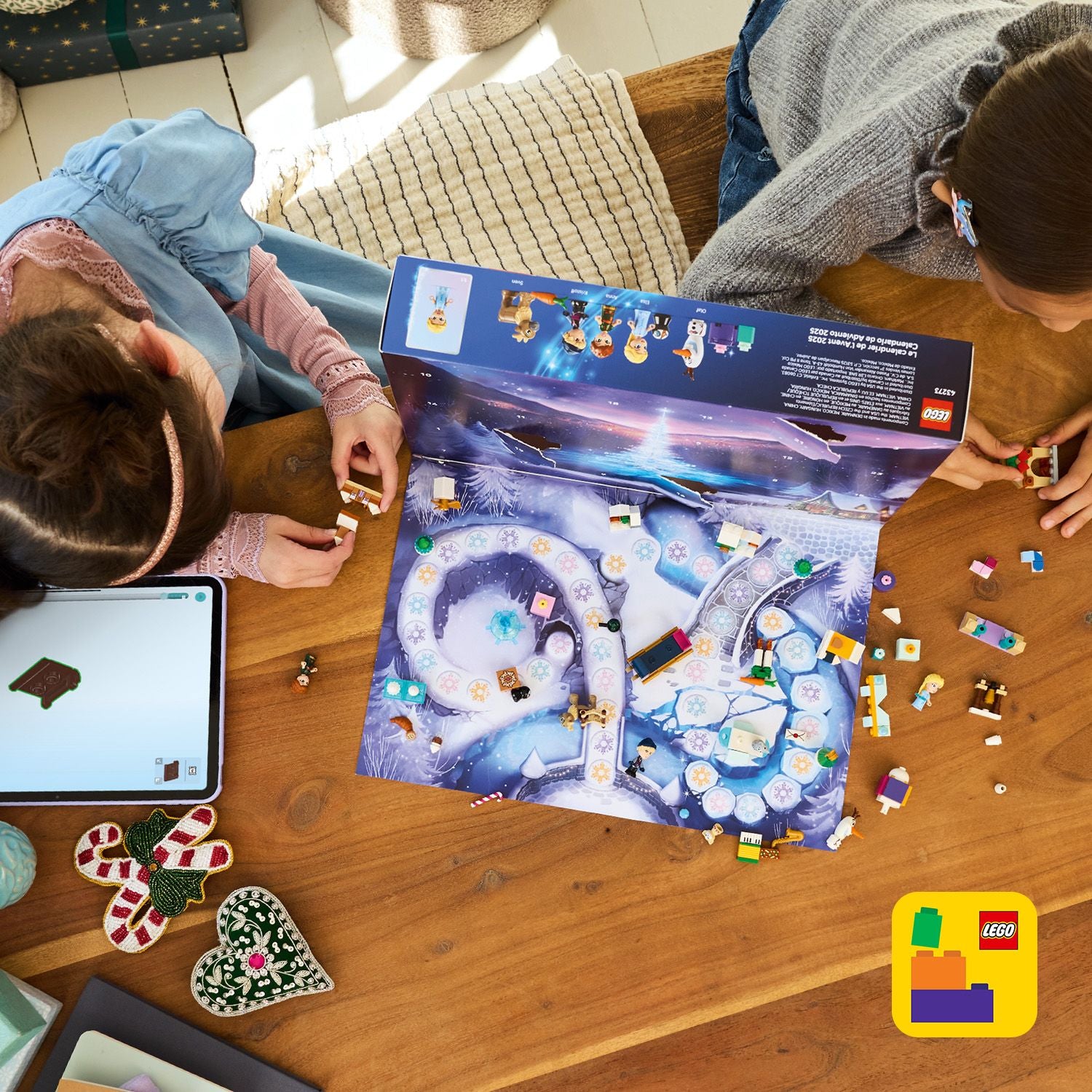 2 Kinder sitzen an einem Tisch, Bild von oben. Sie spielen mit dem Adventskalender, neben ihnen liegt ein Tablet.