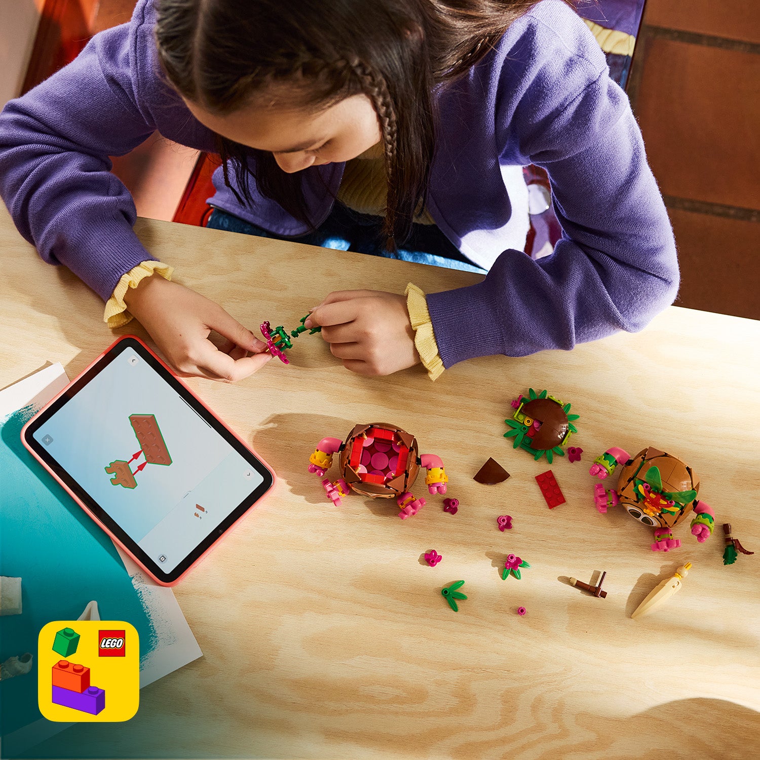 Kind baut mit LEGO Kakamora-Figuren und -Teilen auf einem Holztisch neben einem Tablet mit Bauanleitung