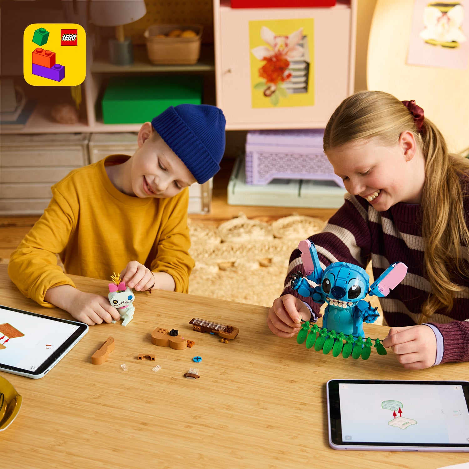 Zwei Kinder sitzen an einem Holztisch und bauen LEGO Figuren von Stitch und Scrump, vor ihnen liegen Tablets mit Bauanleitungen.