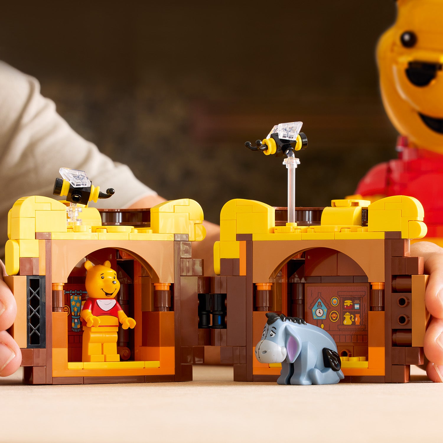 Zwei LEGO Häuser mit gelben Dächern, links steht eine Winnie-Pooh-Figur im Haus, rechts sitzt eine Esel-Figur vor dem Haus mit einer Biene auf dem Dach.