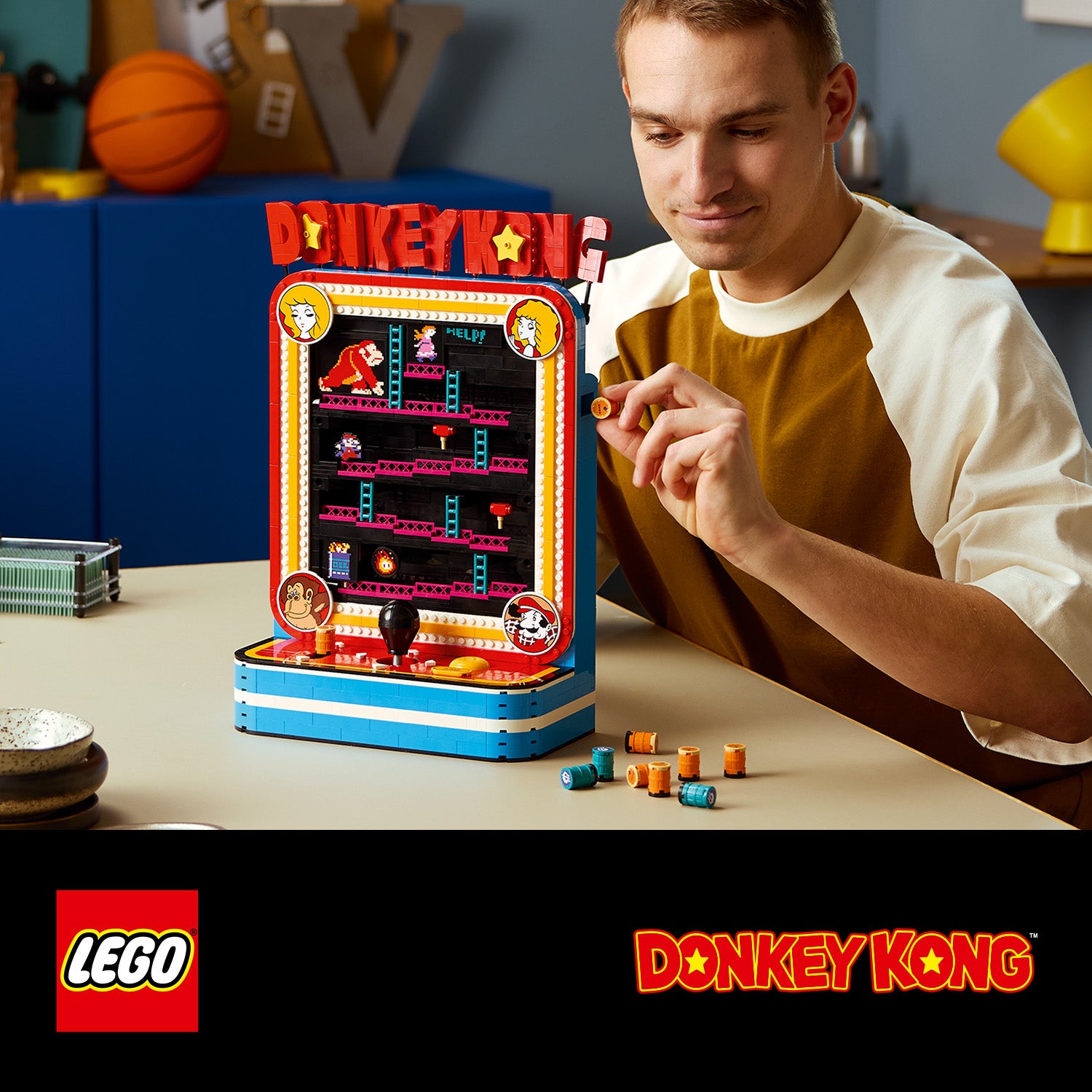 Mann bedient einen kleinen LEGO Donkey-Kong-Arcade-Automaten mit bunten Spielfiguren auf einem Tisch
