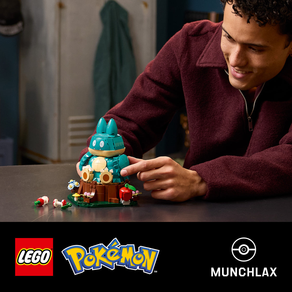 Junger Mann in rotem Pullover spielt mit einem LEGO Modell von Mampfaxo auf einem Tisch
