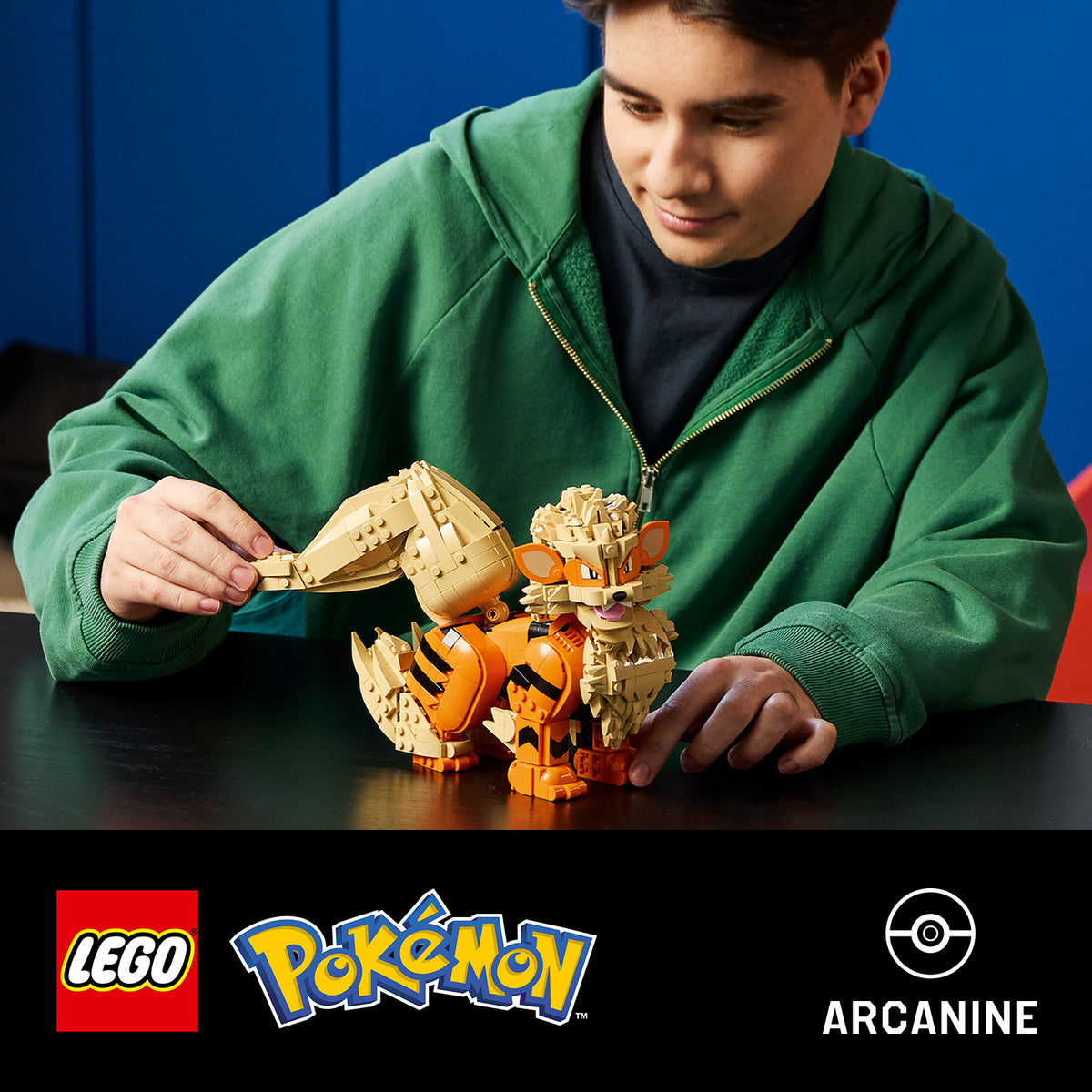 Junge in grünem Kapuzenpullover spielt mit einem LEGO Modell des Pokémon Arkani auf einem schwarzen Tisch