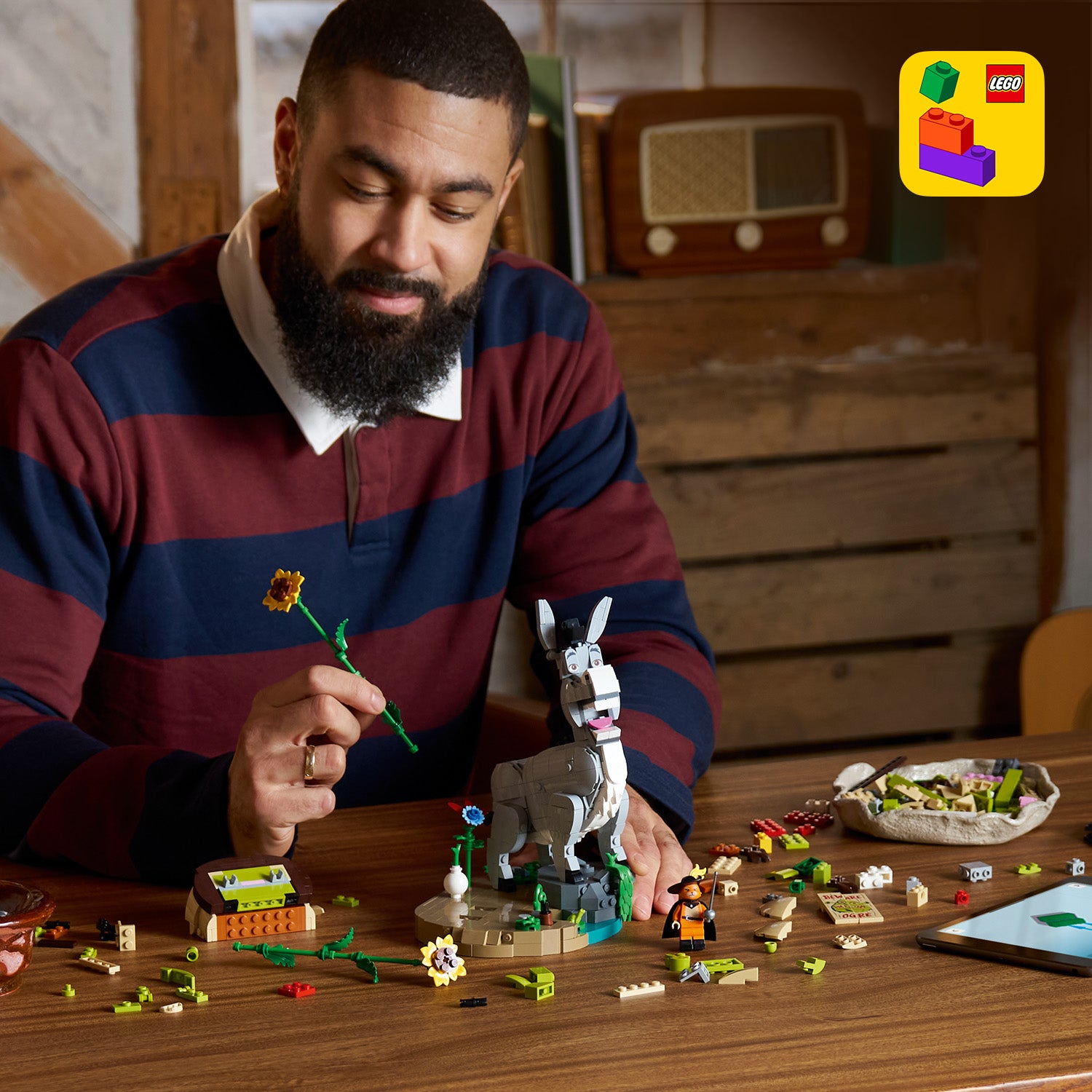 Person mit gestreiftem Pullover sitzt an einem Holztisch und baut LEGO Figuren von Esel und dem gestiefelten Kater aus dem LEGO Shrek-Set