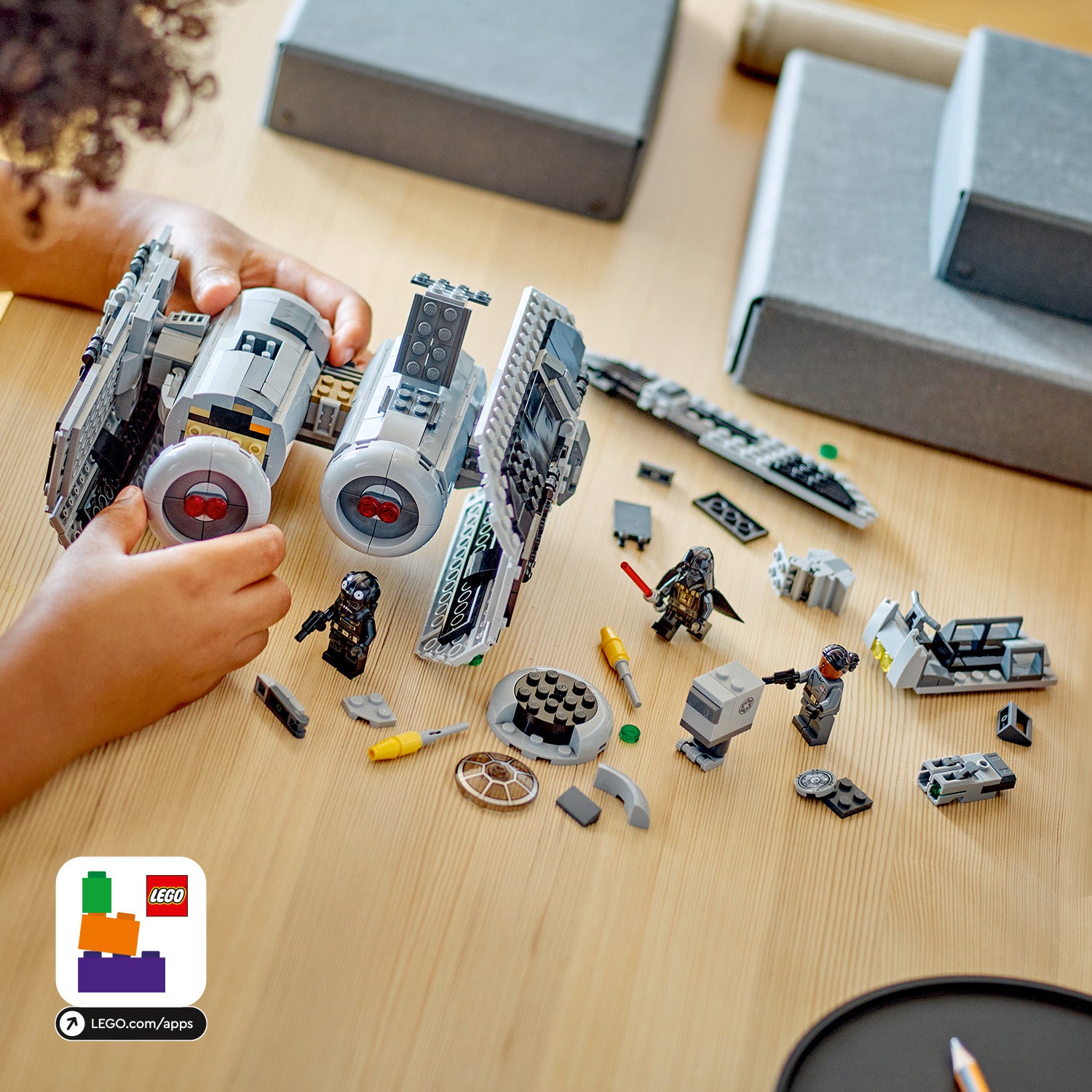 Kind hält ein zusammengebautes LEGO Star Wars TIE Bomber Modell, umgeben von verstreuten LEGO-Teilen und Minifiguren auf einem Holztisch