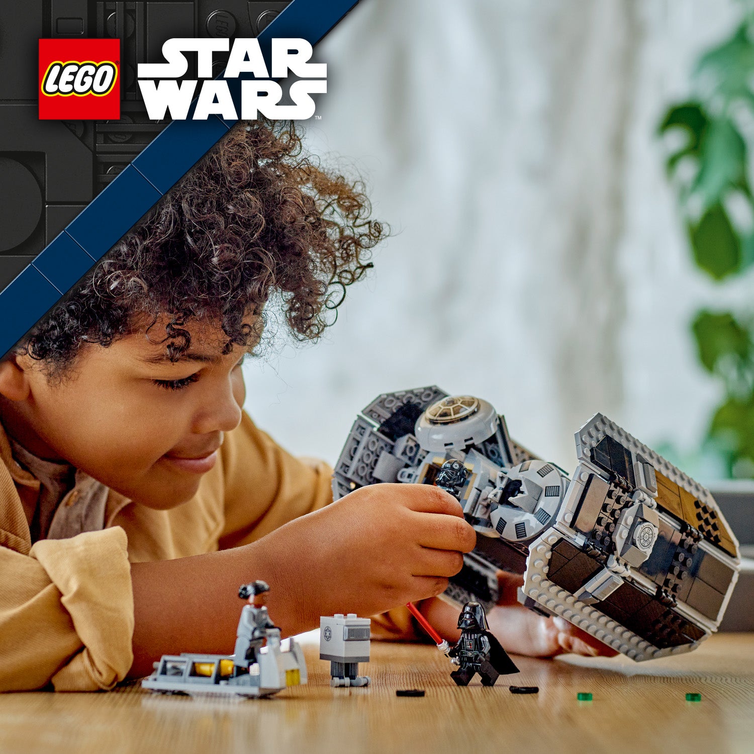 Kind spielt mit einem LEGO Star Wars TIE Bomber Modell und mehreren Minifiguren auf einem Holztisch im Innenraum.