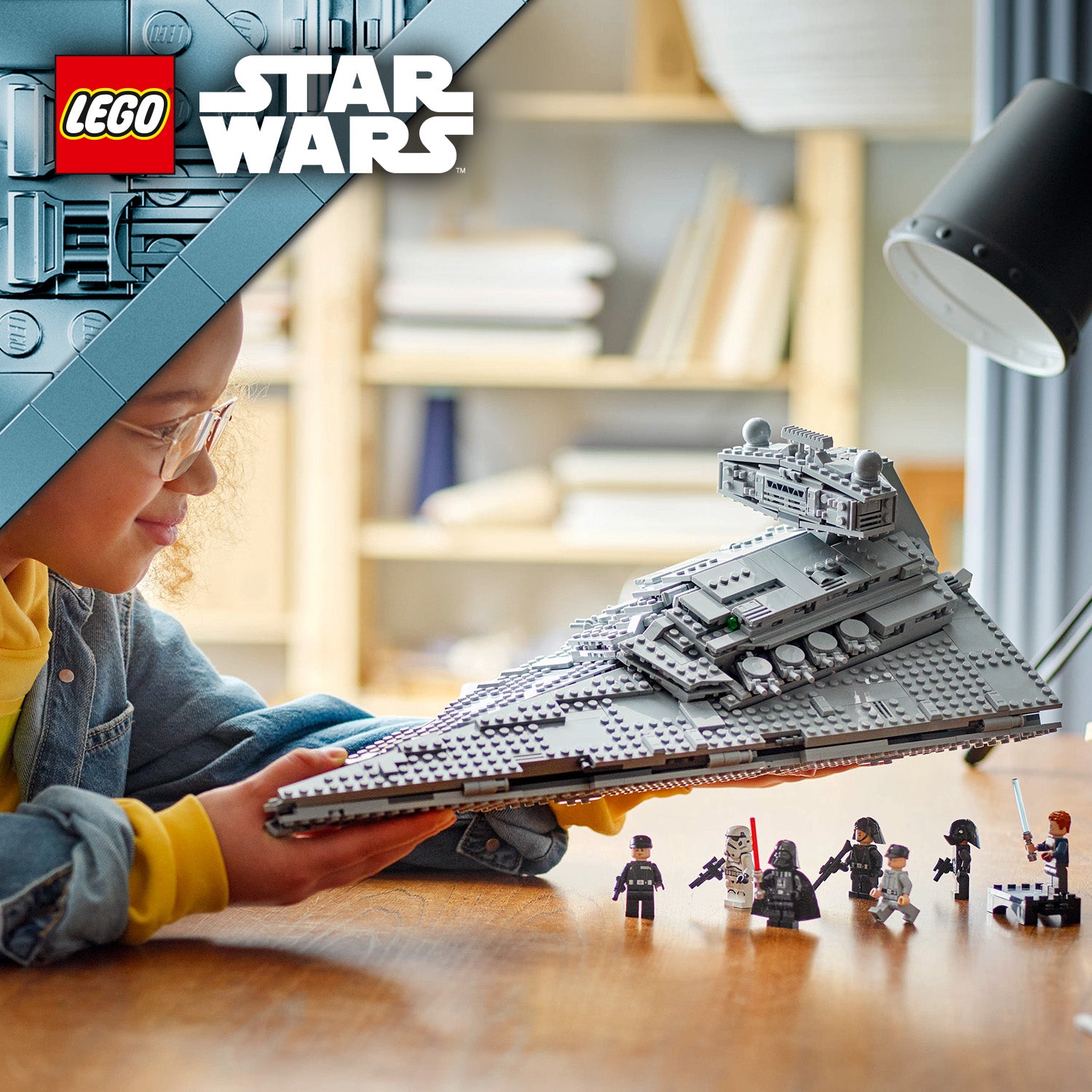 Kind hält ein LEGO Star Wars Modell des imperialen Sternenzerstörers über einem Holztisch mit mehreren LEGO Star Wars Minifiguren im Vordergrund