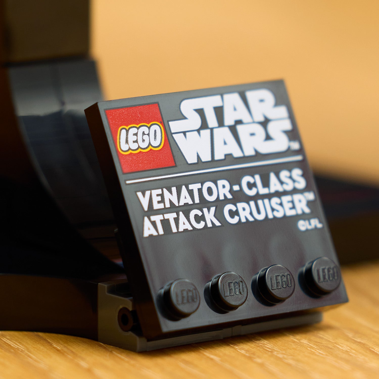 Schwarzes LEGO Schild mit den Logos von LEGO und Star Wars sowie dem Text 'VENATOR-CLASS ATTACK CRUISER' auf einer Holzoberfläche.