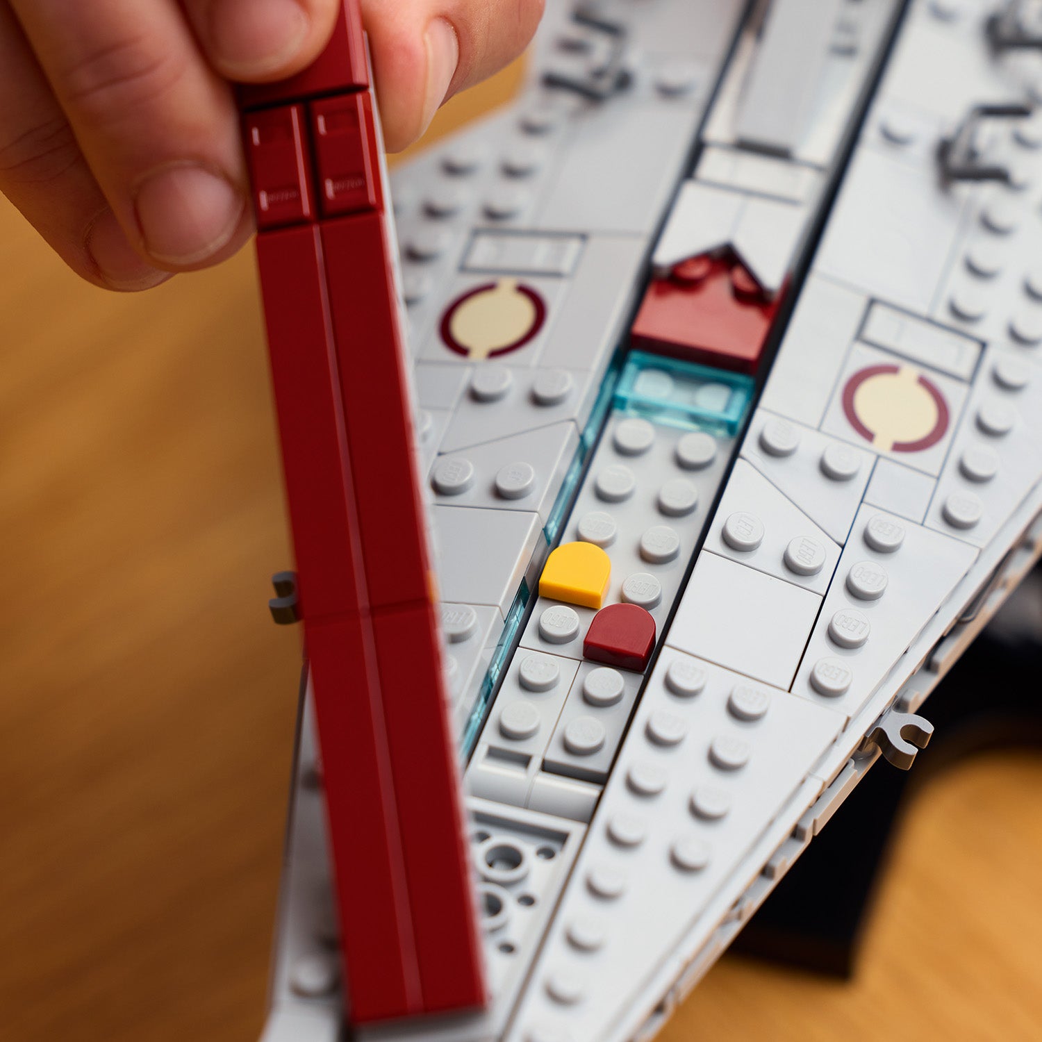Nahaufnahme eines LEGO Star Wars Angriffskreuzers der Venator-Klasse mit einer Hand, die ein langes rotes LEGO Teil anbringt.