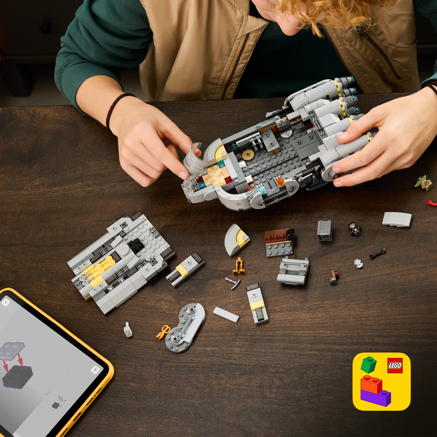 Person baut ein LEGO Star Wars Sternenschiff der Anzellaner aus grauen und gelben Bausteinen auf einem Holztisch zusammen, daneben liegen weitere Bauteile und ein Tablet mit Bauanleitung.