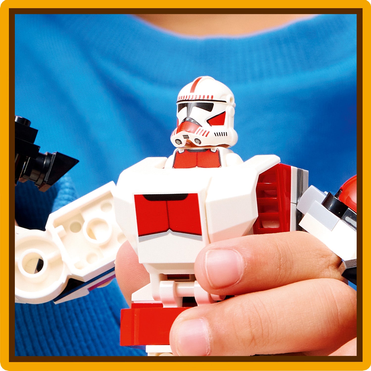 Nahaufnahme einer Hand, die eine LEGO Star Wars-Figur des Klon-Schocktruppen-Mechs hält, erkennbar an weiß-roter Rüstung und Helm mit Visier.