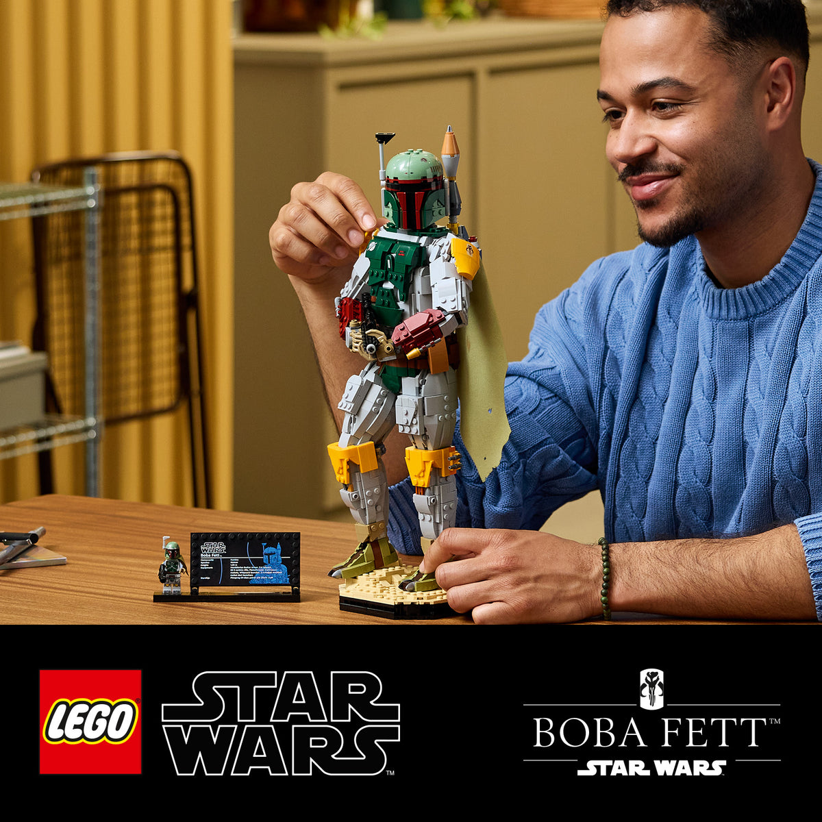 Mann in blauem Pullover baut eine LEGO Statue von Boba Fett aus Star Wars auf einem Tisch