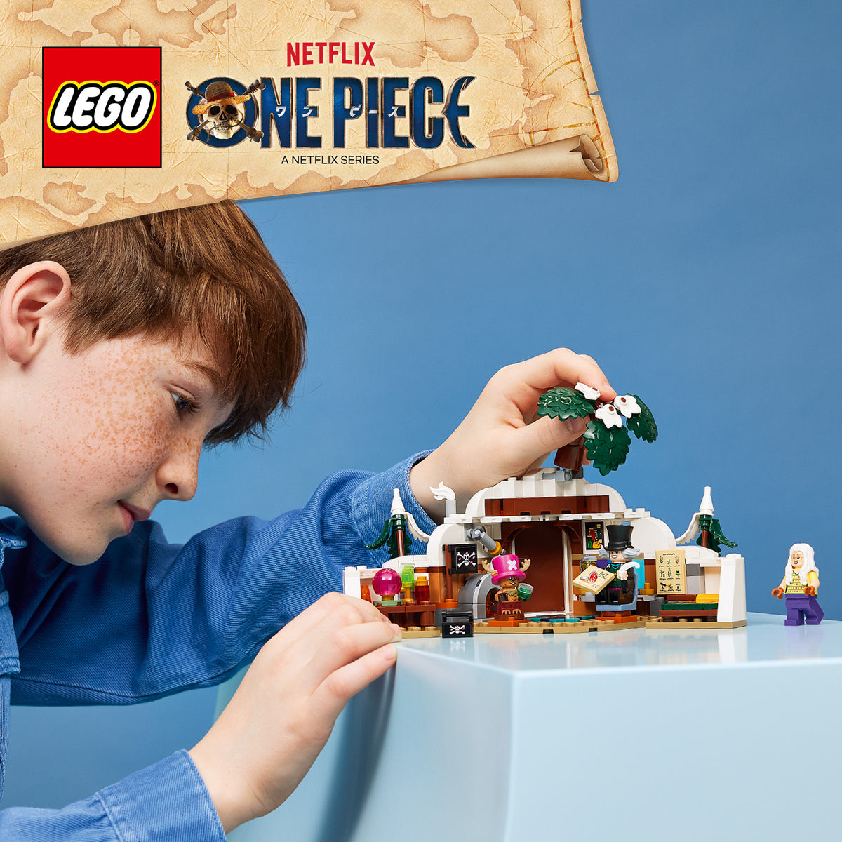 Junge baut mit LEGO Steinen ein kleines Haus mit Palmen und Figuren aus der Serie One Piece