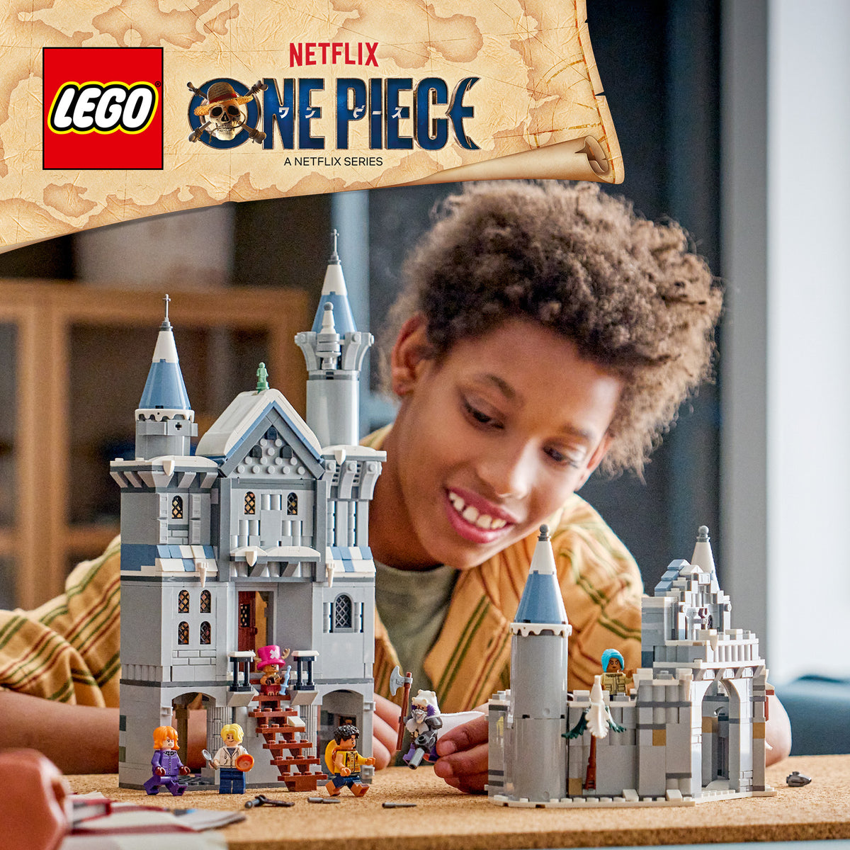Kind spielt mit LEG -Set "Duell im Schloss Drumm" aus der Serie LEGO One Piece, das zwei graue Burgtürme mit blauen Dächern und mehreren Minifiguren zeigt