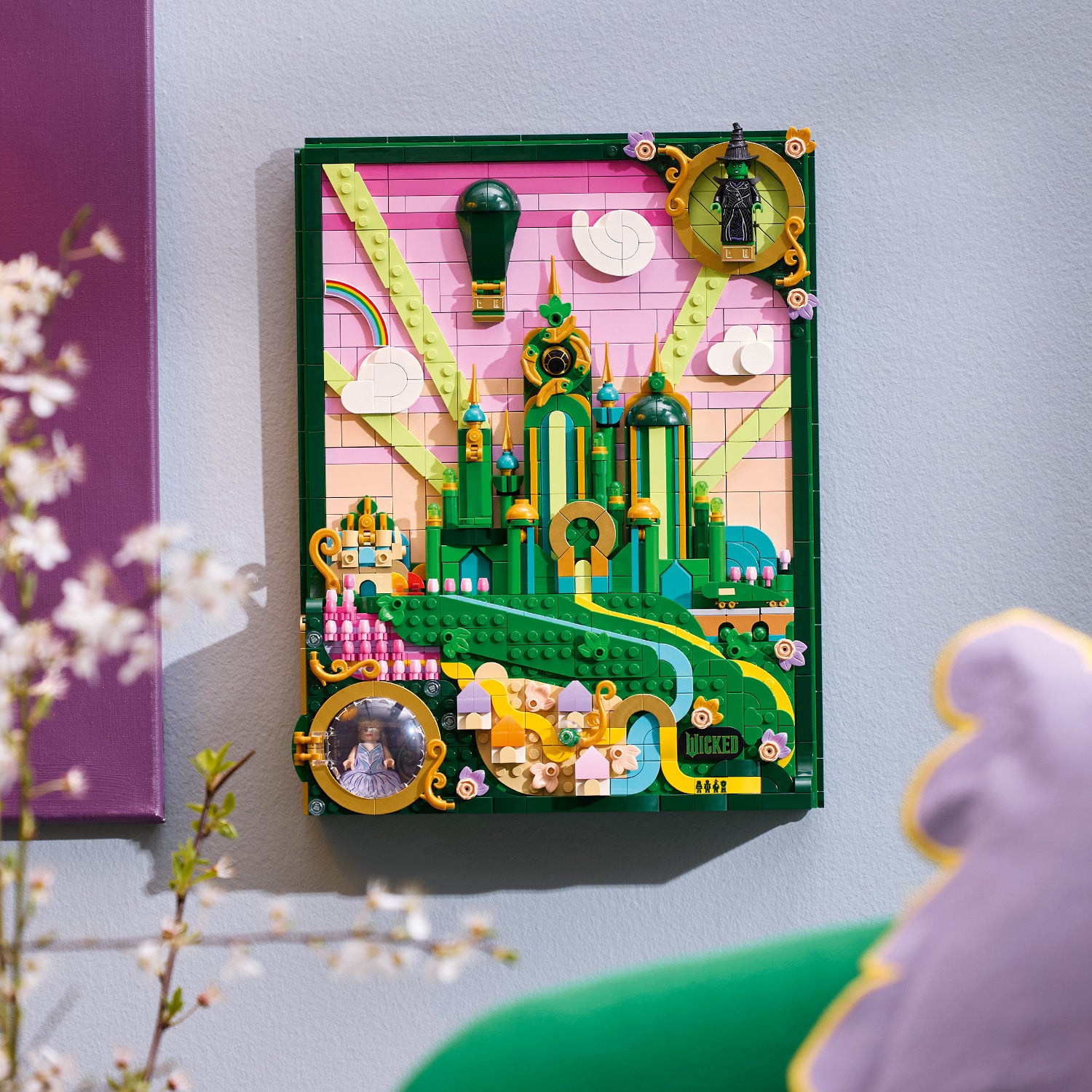LEGO Wandkunst mit einer grünen Stadtlandschaft vor rosa Himmel, Wolken, Regenbogen und Heißluftballon, verziert mit goldenen Ornamenten und einem kleinen Spiegel