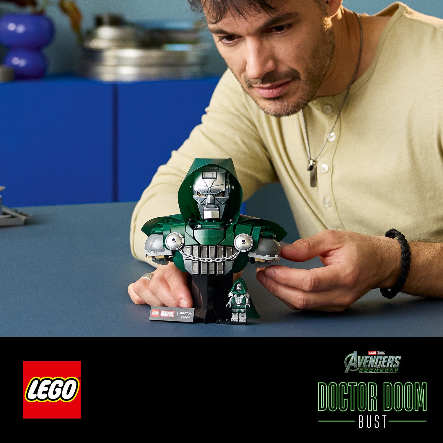 Mann baut eine LEGO Büste von Doctor Doom mit grünem Umhang und silberner Maske auf einem Tisch